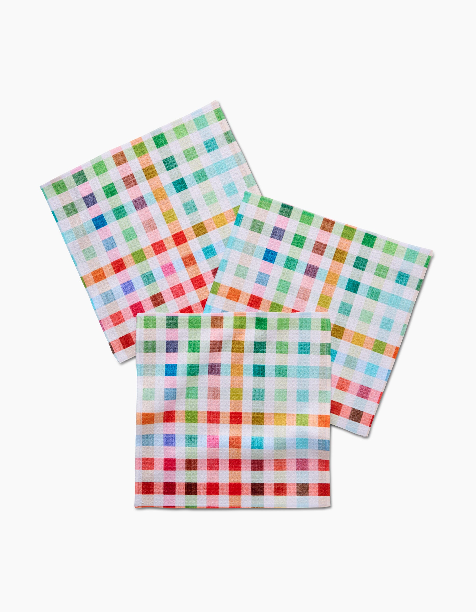 Three folded Pascale Dilger Woven Spring Plaid napkins, made from recycled materials, feature a vibrant red, green, blue, and orange checkered pattern and are arranged overlapping on a white background.