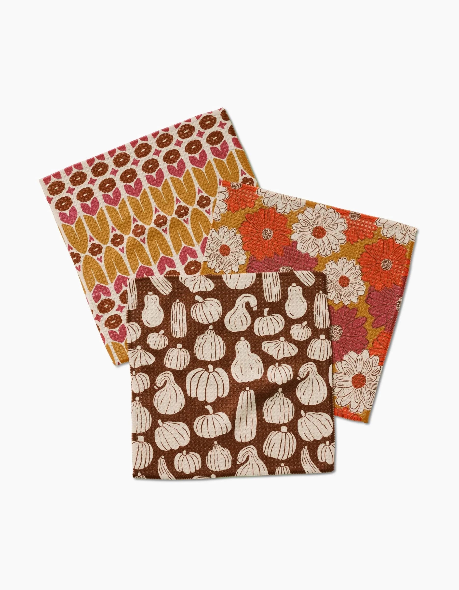 The Zinnia Forever set by Kayla Ann includes three Geoweave cloth napkins with patterns of white pumpkins on brown, orange and white flowers, and red, pink, and yellow leaves on cream backgrounds.