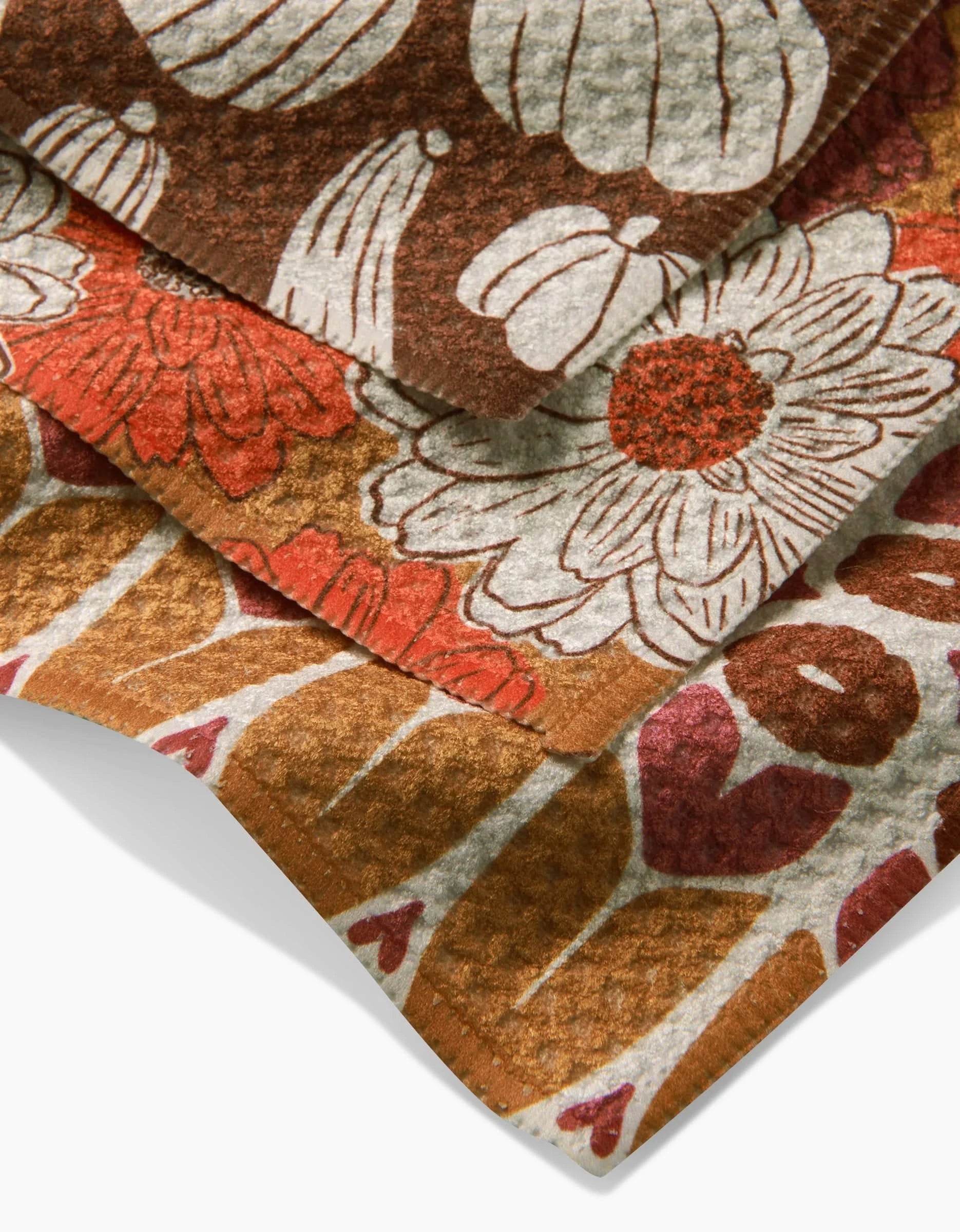 The Kayla Ann Zinnia Forever set includes three overlapping dishcloths made from recycled materials, featuring retro-inspired floral and leaf designs in brown, orange, red, and white.