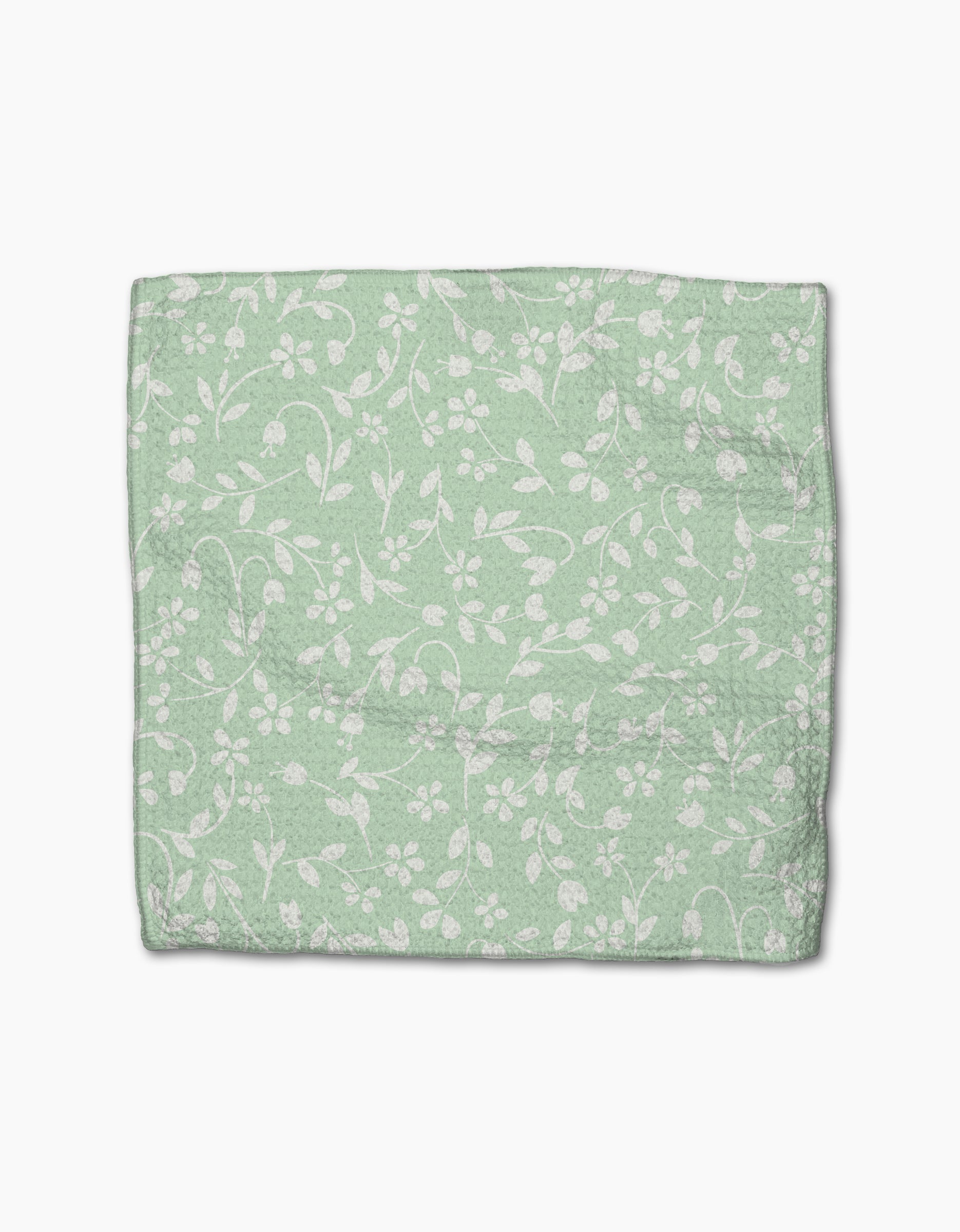 The GEOMETRY Dandy is a light green dishcloth made from Geoweave fabric, featuring a subtle white floral and vine pattern. It is shown folded on a plain white background.