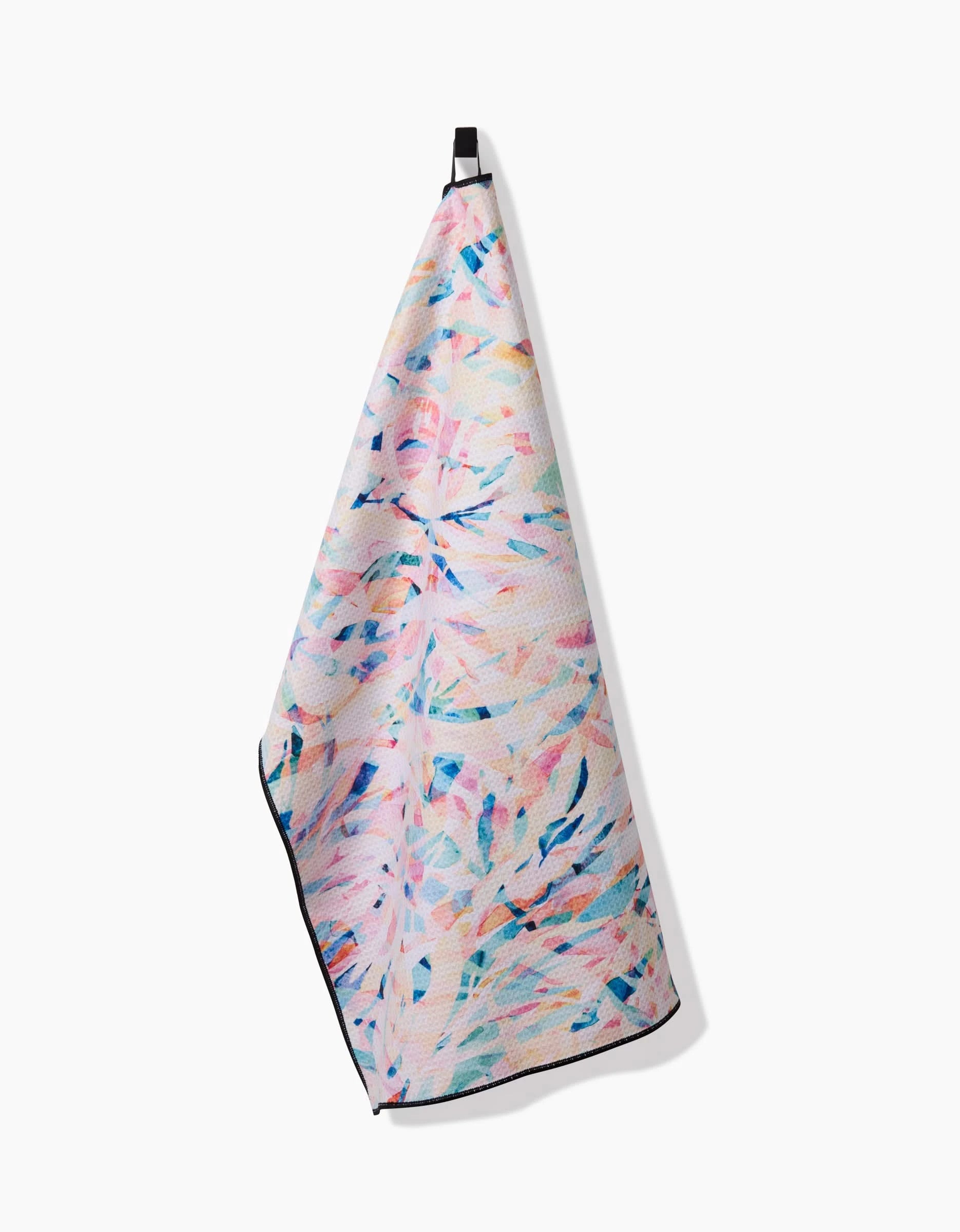 The Rachel Parker Abstract Jungle towel, featuring a pastel abstract leaf design in pink, blue, and purple, hangs from a black loop against a white background.