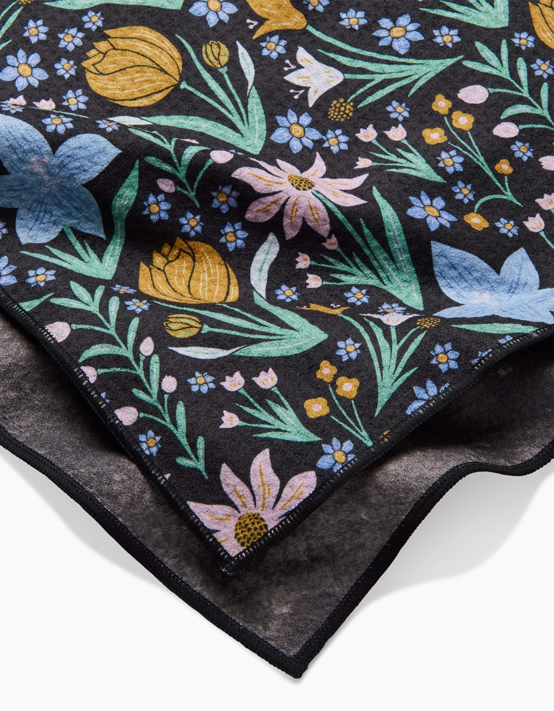 A close-up of Danelys Sidron’s Garden of Light fabric, folded against a black background, displays its colorful floral pattern—yellow, pink, and blue flowers with green leaves. The visible edge highlights its absorbency—ideal for Dog Towels.