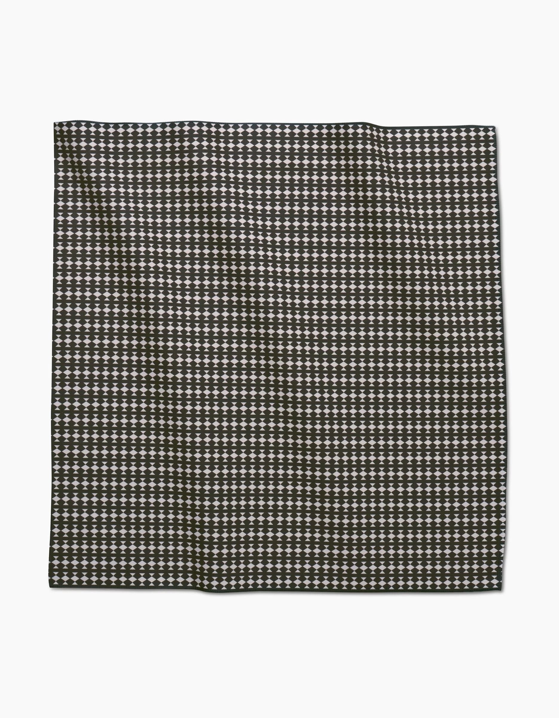 A neatly folded GEOMETRY Maori dinner napkin made from Geosuede fabric, showcasing a black-and-white houndstooth pattern, is displayed against a plain white background.