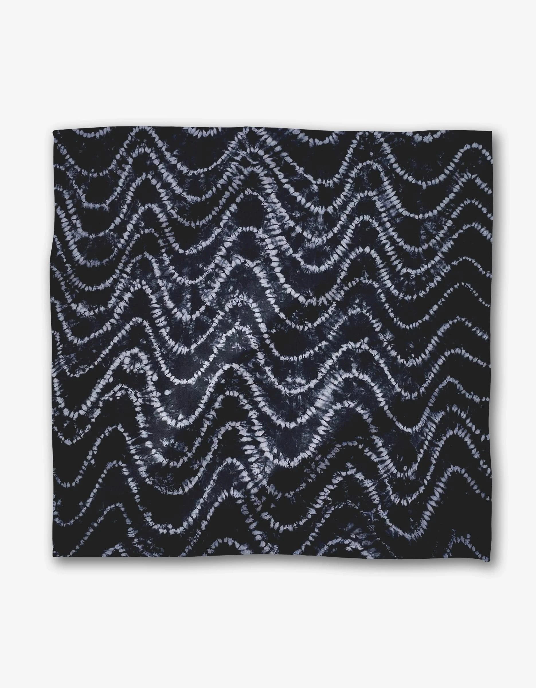 The Shibo Dinner Napkin Set by GEOMETRY features rectangular Geosuede fabric with a dark background and white and light blue wavy, zigzag tie-dye patterns.