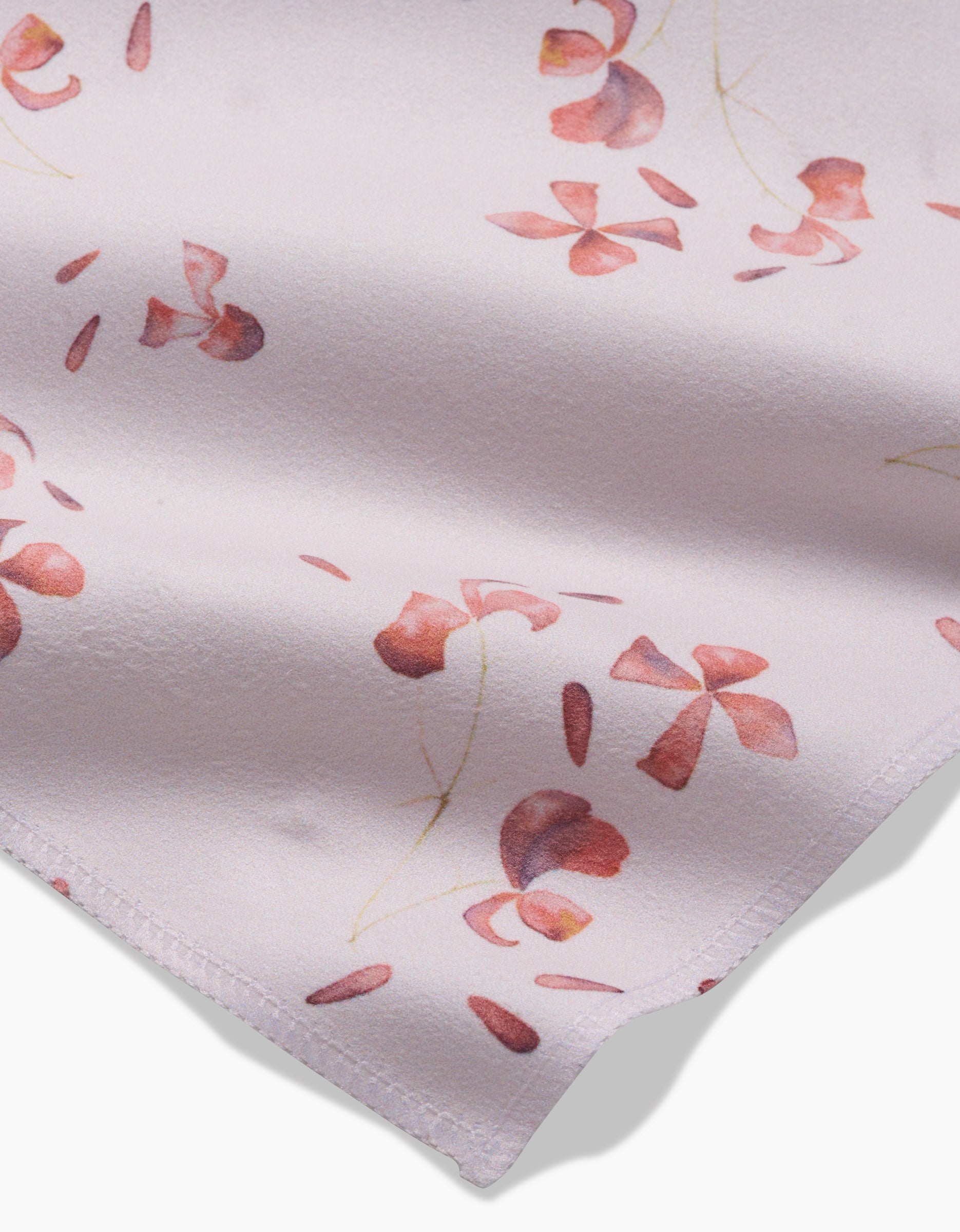 A close-up of GEOMETRYs Tiny Petals shows soft, light pink Geosuede fabric adorned with delicate red and pink floral patterns featuring curved stems and petals, with the fabric’s edge visible in the lower corner.