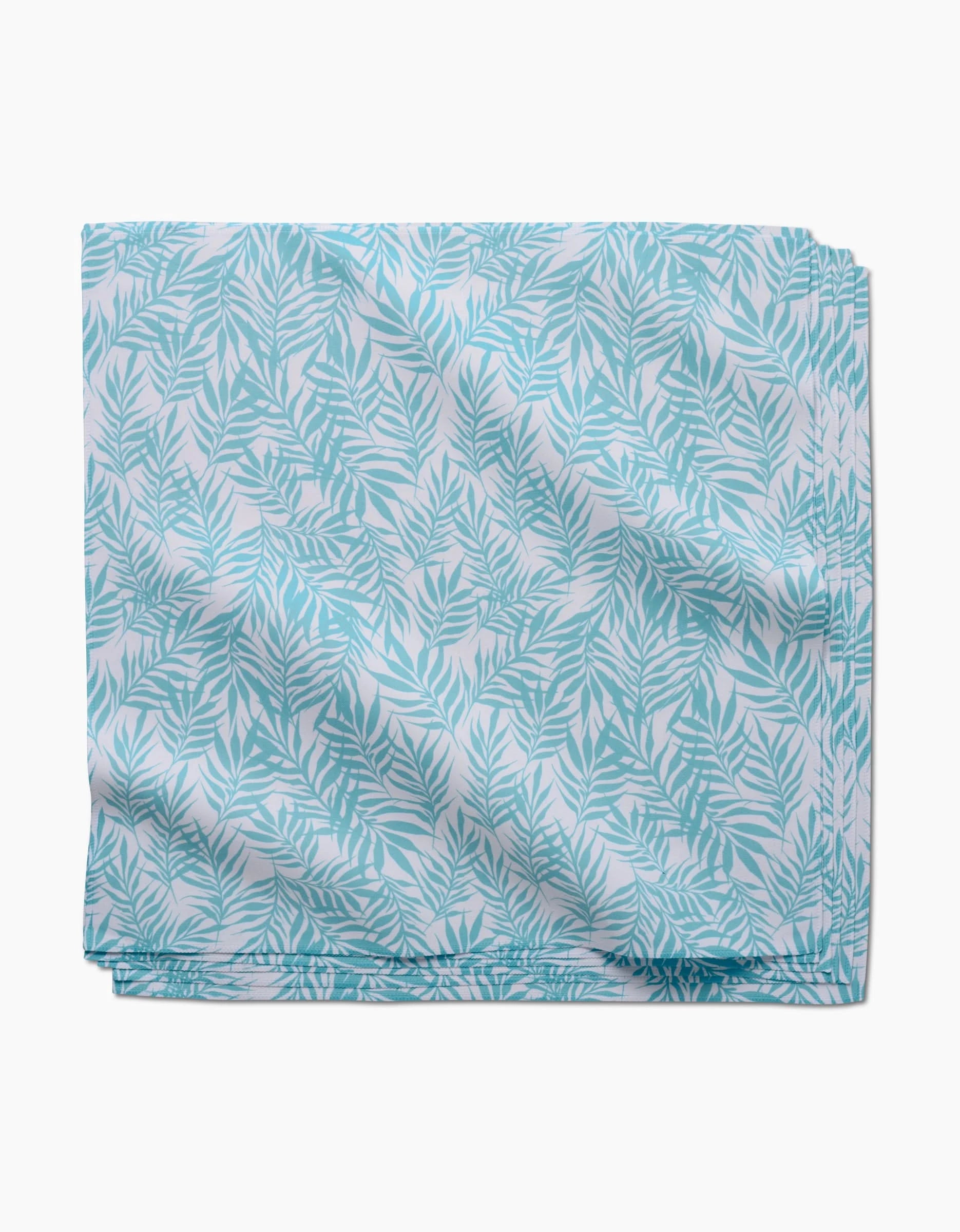 The Aqua Branches by GEOMETRY features a folded fabric with a light blue and white leafy pattern, showcasing fern-like leaves on a smooth surface—ideal for reusable, eco-friendly napkins.