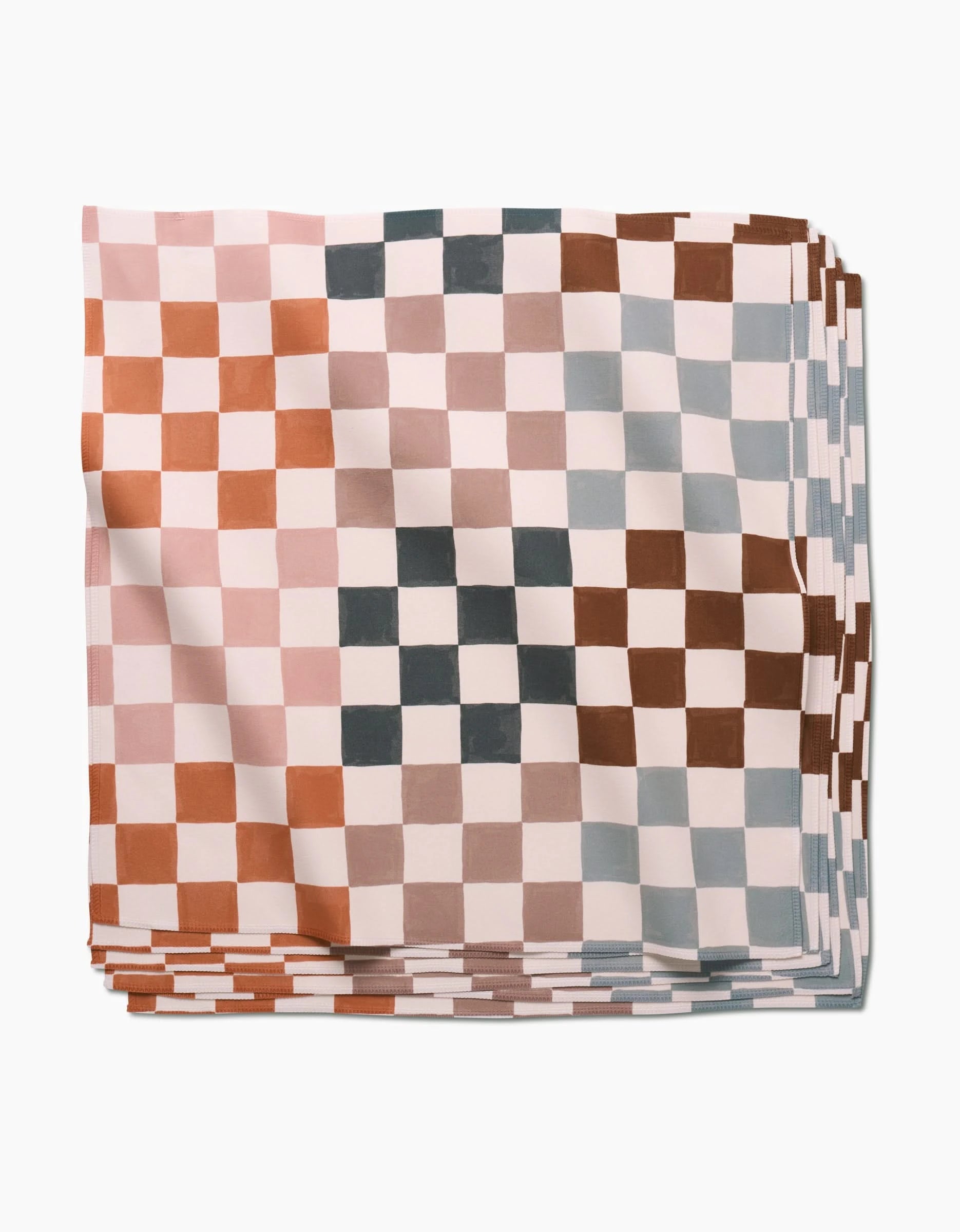 A neatly folded stack of GEOMETRY Autumn Checkers Dinner Napkins, showcasing a checkered pattern in muted pink, brown, gray, and white tones, made from recycled materials and set against a white background.
