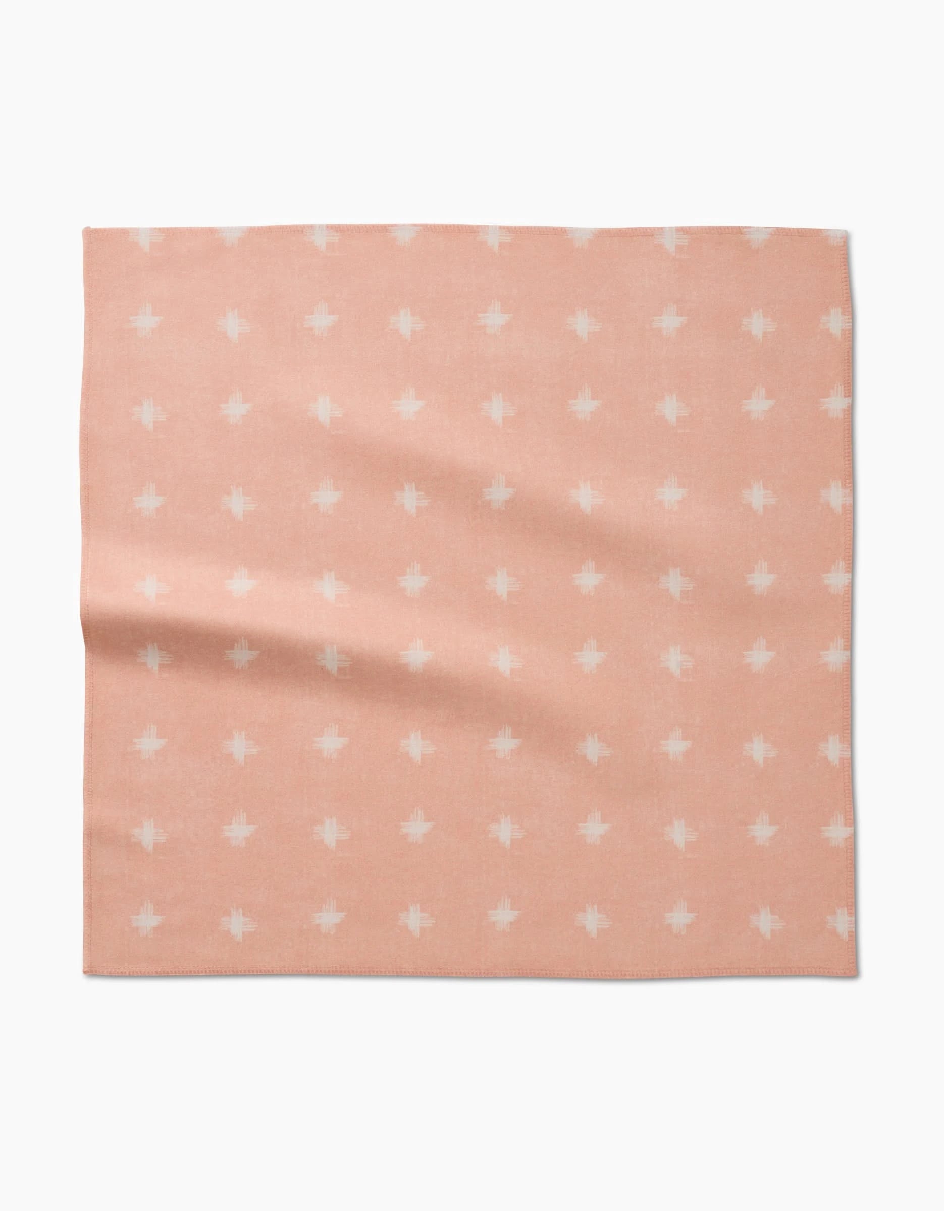The Aveline Dinner Napkin by Amy MacCready is a square, light pink Geosuede napkin with small white geometric crosses arranged in a grid, shown flat against a white background.
