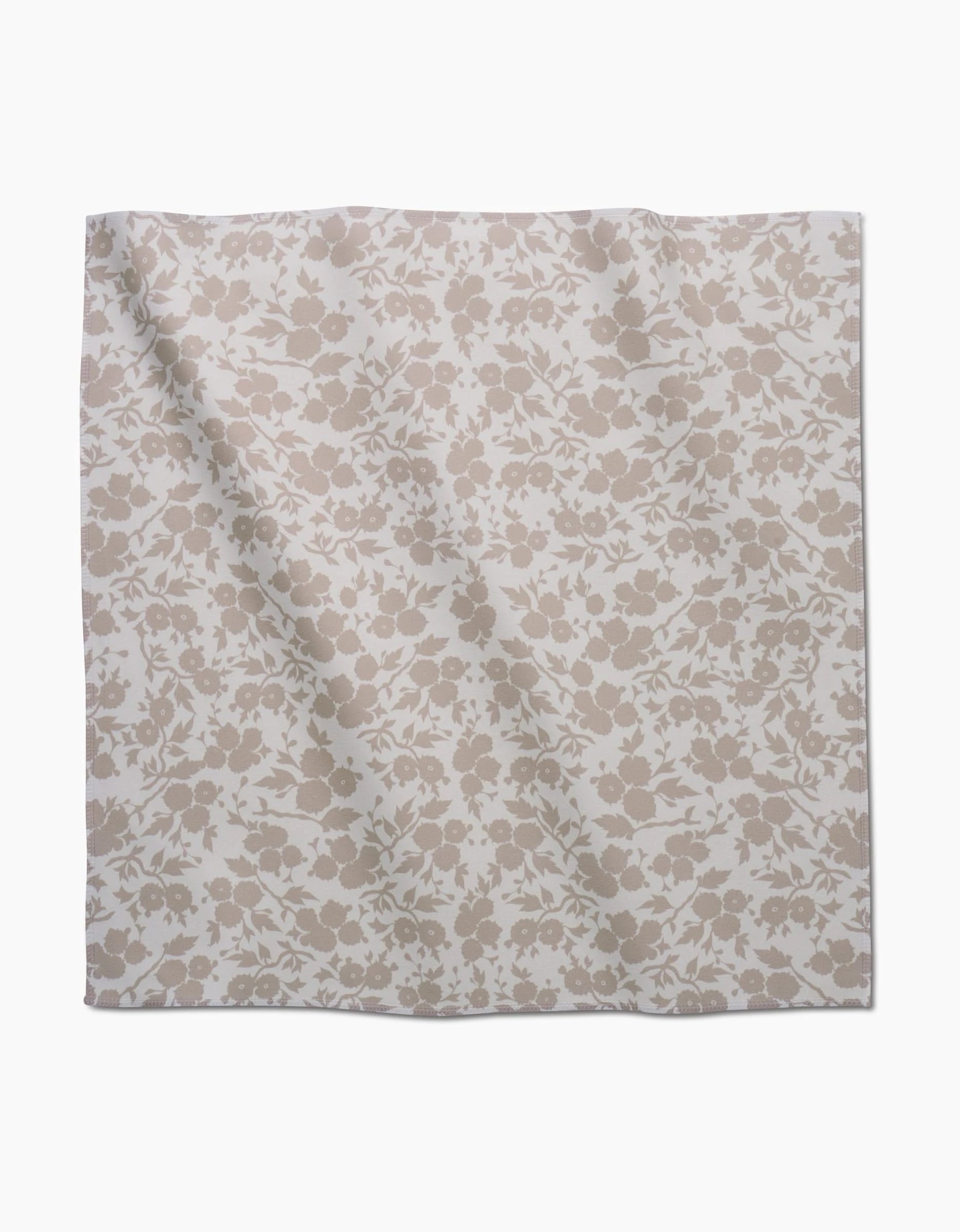 The GEOMETRY Bettys Buds napkin is a square cloth made from recycled Geosuede, showcasing a light beige floral pattern with assorted flowers and leaves on a white background.