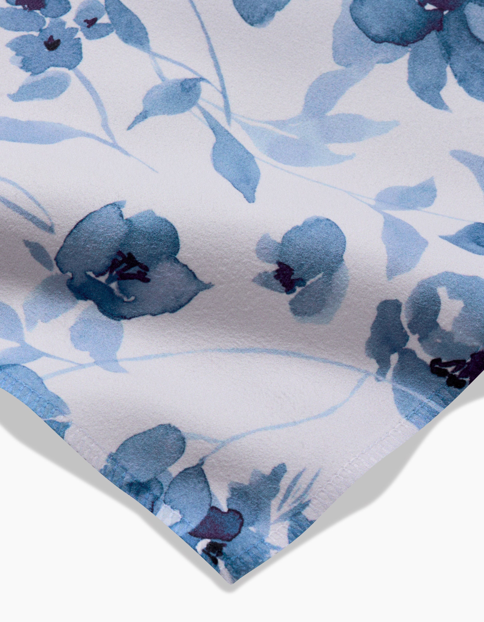 Close-up of Aubrey Fairchilds Blue Floral Geosuede fabric with a light background and blue watercolor-style flowers and leaves. The soft, abstract floral pattern is visible, along with the fabric’s edge in the bottom left corner.