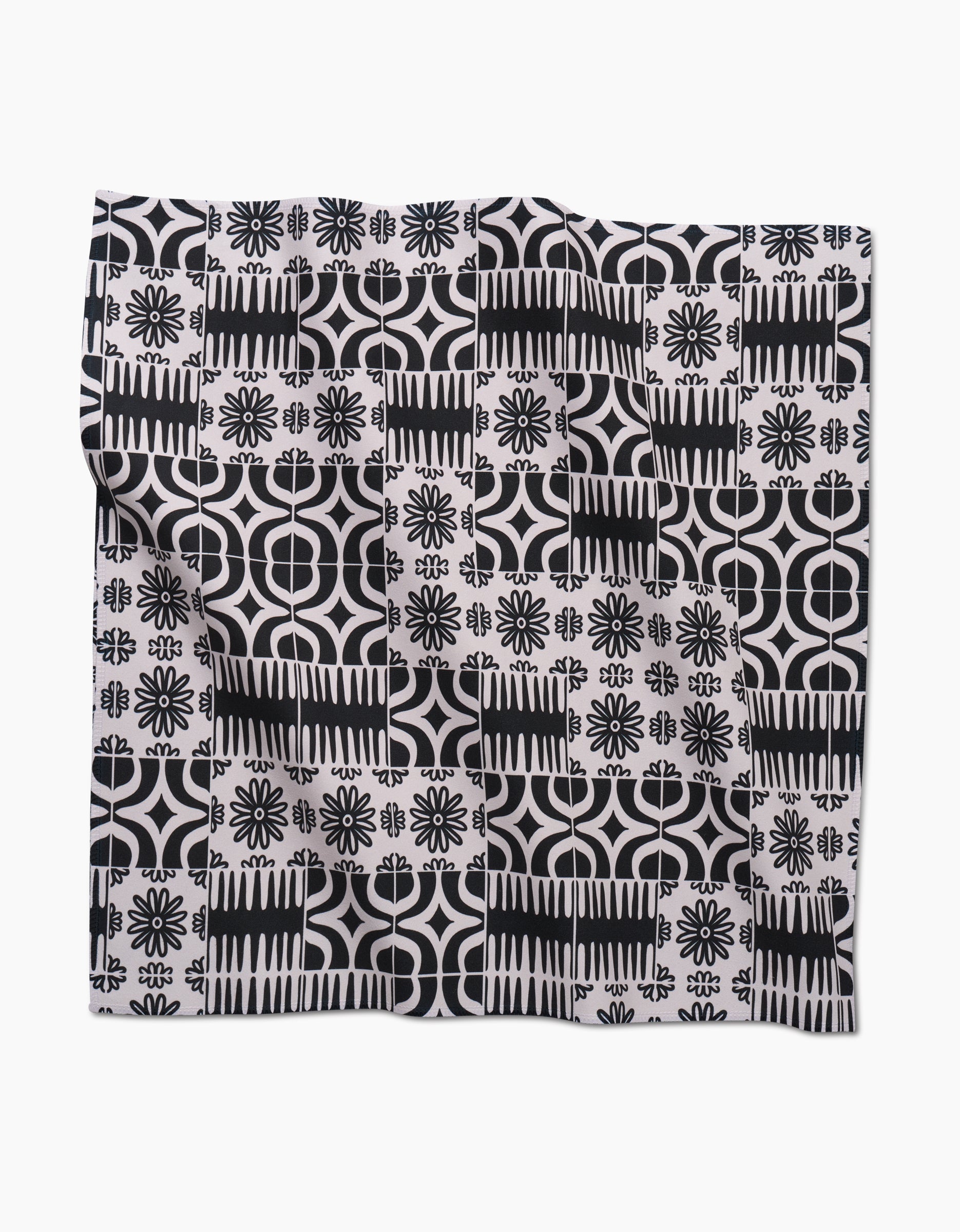 The Bohemian Mosaic by GEOMETRY is a square dinner napkin set made from Geosuede fabric, featuring a black and white geometric and floral tile pattern with rows of flowers, circles, and abstract shapes on a white background.
