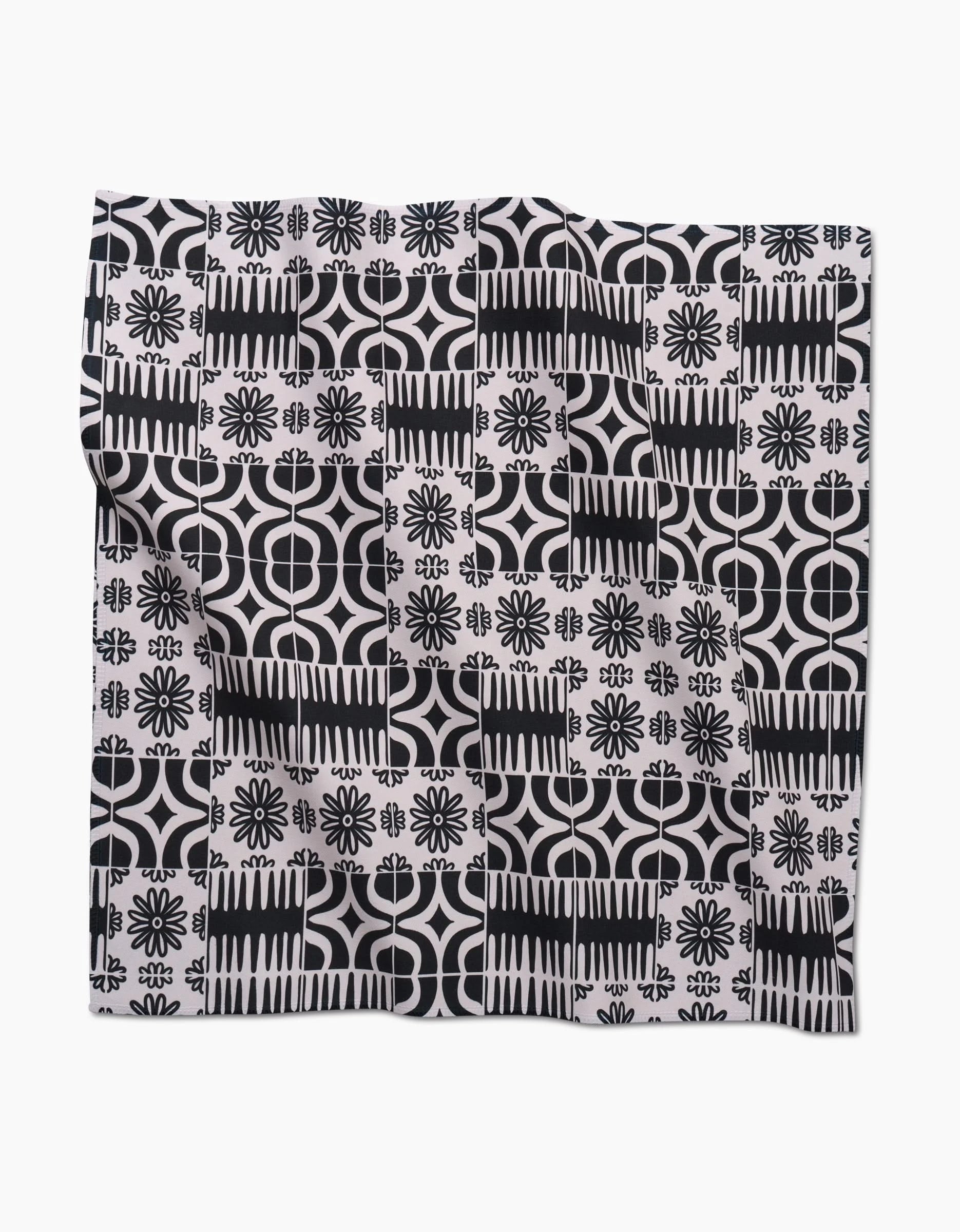 The Bohemian Mosaic by GEOMETRY is a square dinner napkin set made from Geosuede fabric, featuring a black and white geometric and floral tile pattern with rows of flowers, circles, and abstract shapes on a white background.