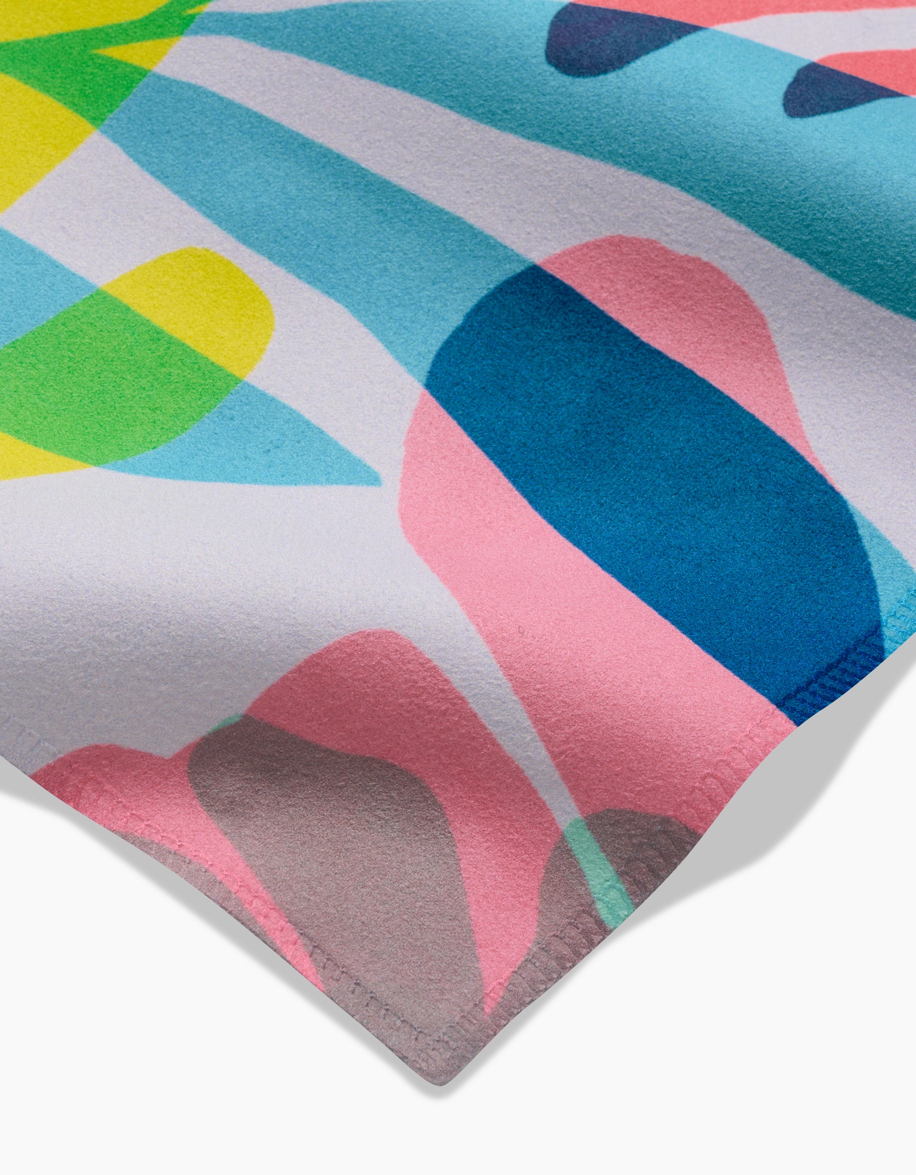 A close-up of GEOMETRY’s Botanical Burst Geosuede Dinner Napkin, showcasing an abstract, colorful pattern with pink, blue, yellow, green, and gray organic shapes on white. Made from recycled materials with neatly stitched corners.