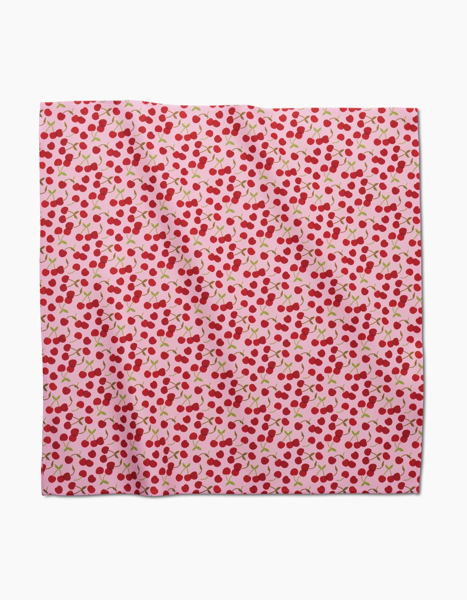 The GEOMETRY Cheery Cherries is a square pink dinner napkin made from soft Geosuede fabric, decorated with small red cherries and green stems scattered evenly across the surface.
