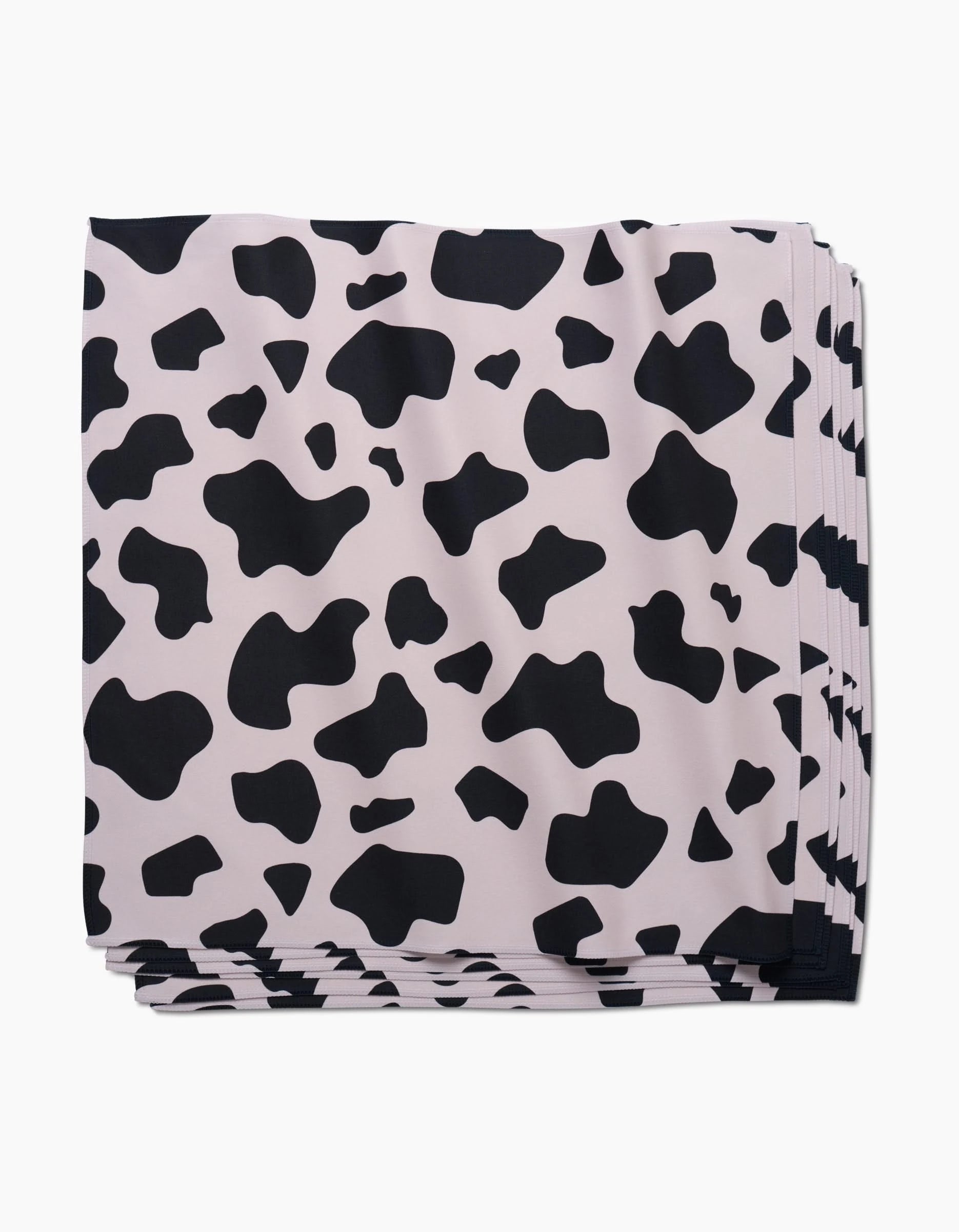 A stack of GEOMETRYs Cow Print Black Dinner Napkin Set, made from eco-friendly Geosuede fabric and featuring an irregular black and white cow print pattern.