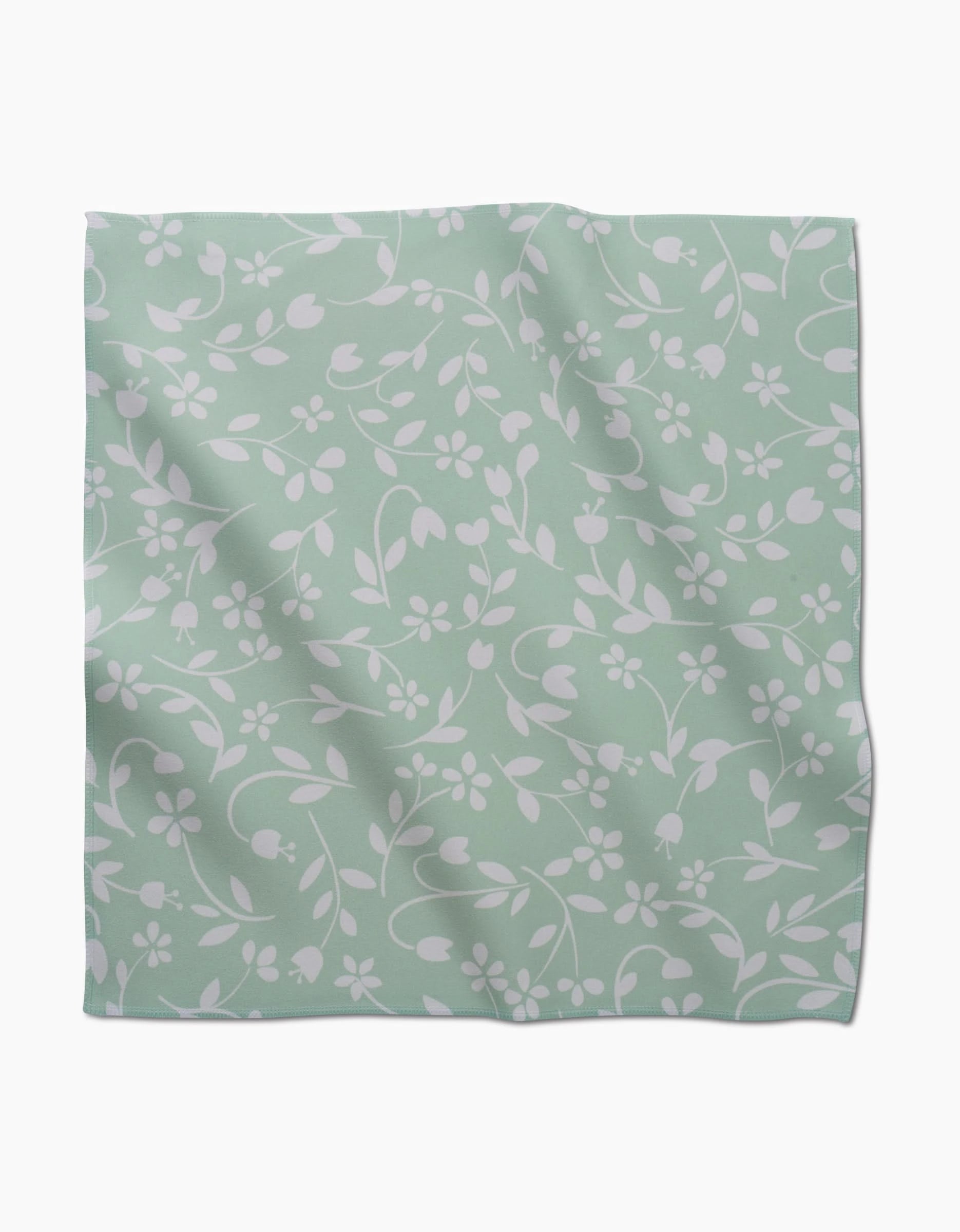 The Dandy by GEOMETRY is a light green, square dinner napkin with a white floral and leaf pattern. Made from recycled fabric, it features soft folds, subtle texture, and an absorbent feel.