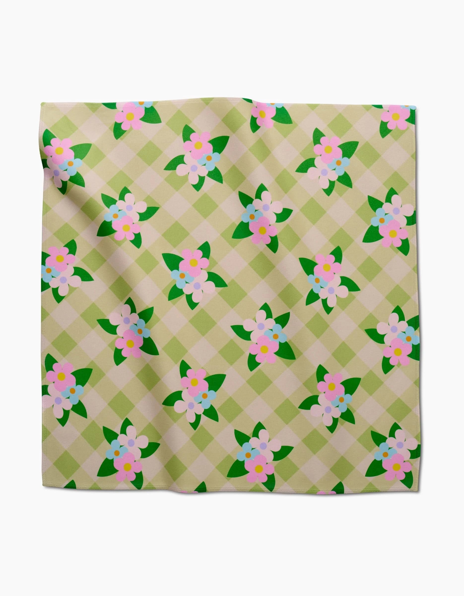 The GEOMETRY Doting and Devoted dinner napkin is a square Geosuede fabric featuring a green and beige checkered pattern adorned with pink and white flower clusters and green leaves.