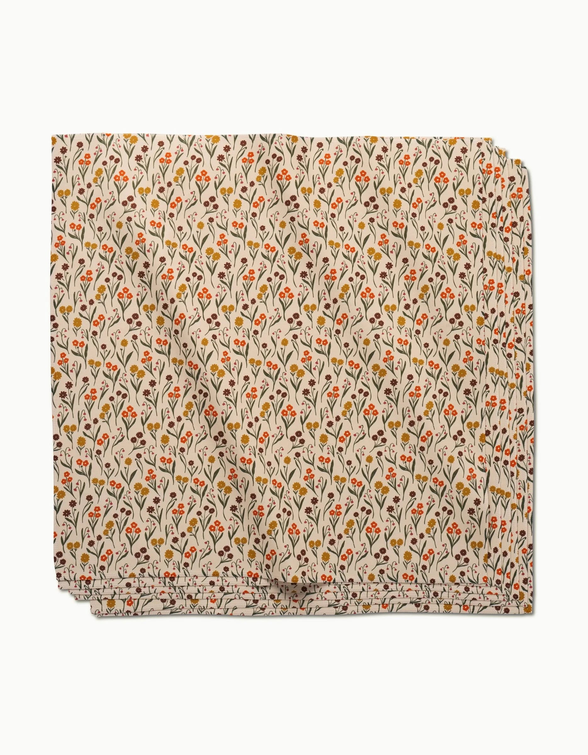 The Fall Blossom dinner napkin by Kayla Ann is crafted from eco-friendly Geosuede using recycled materials. It features a white background with small red, orange, and yellow flowers with green stems in a repeating pattern.