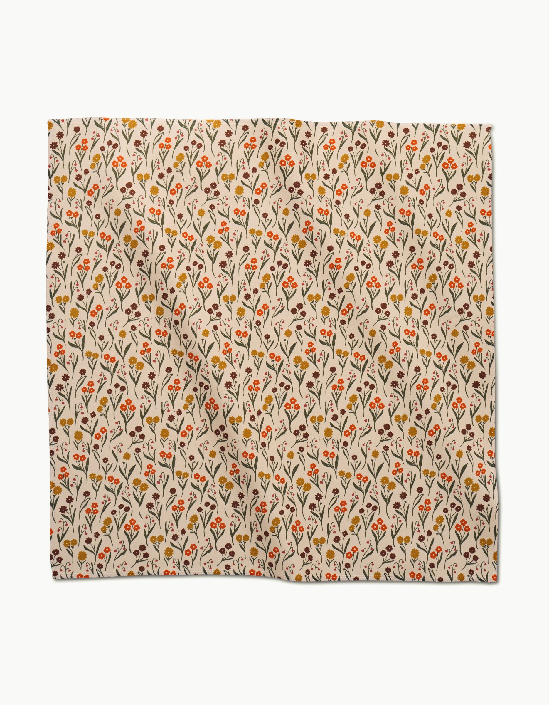 The Fall Blossom dinner napkin by Kayla Ann features beige Geosuede fabric with a repeating pattern of small orange, red, yellow, and brown flowers and leafy vines. The napkin is square-shaped and softly folded with gentle creases.