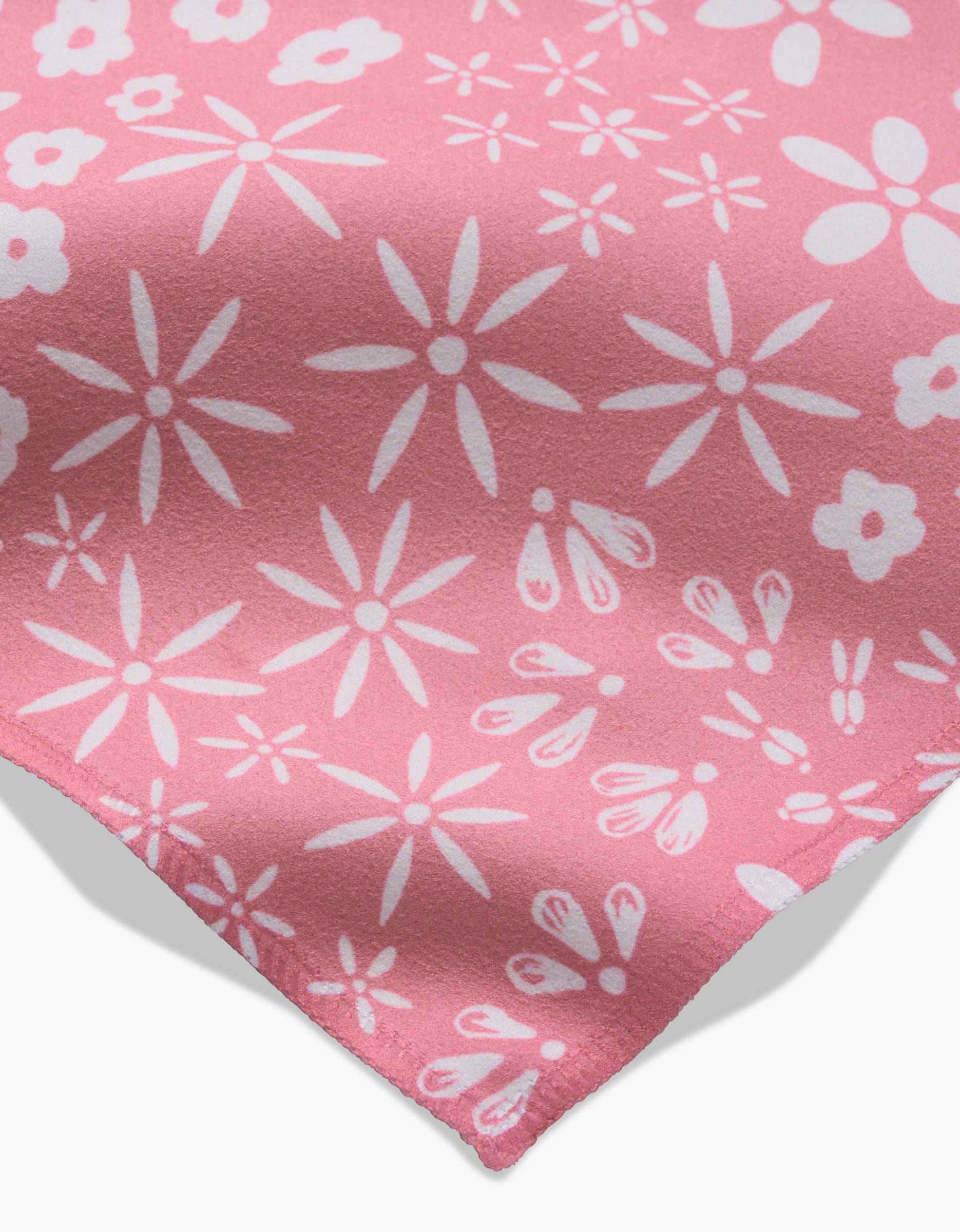 A close-up of the Field of Flowers dinner napkin by Hufton Studio shows its pink Geosuede fabric with white abstract floral shapes and a softly folded corner.