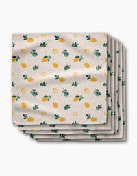 A stack of Sara Mari Freshly Picked Dinner Napkins in Geosuede fabric, featuring yellow lemons, green leaves, and orange dots on a white background.