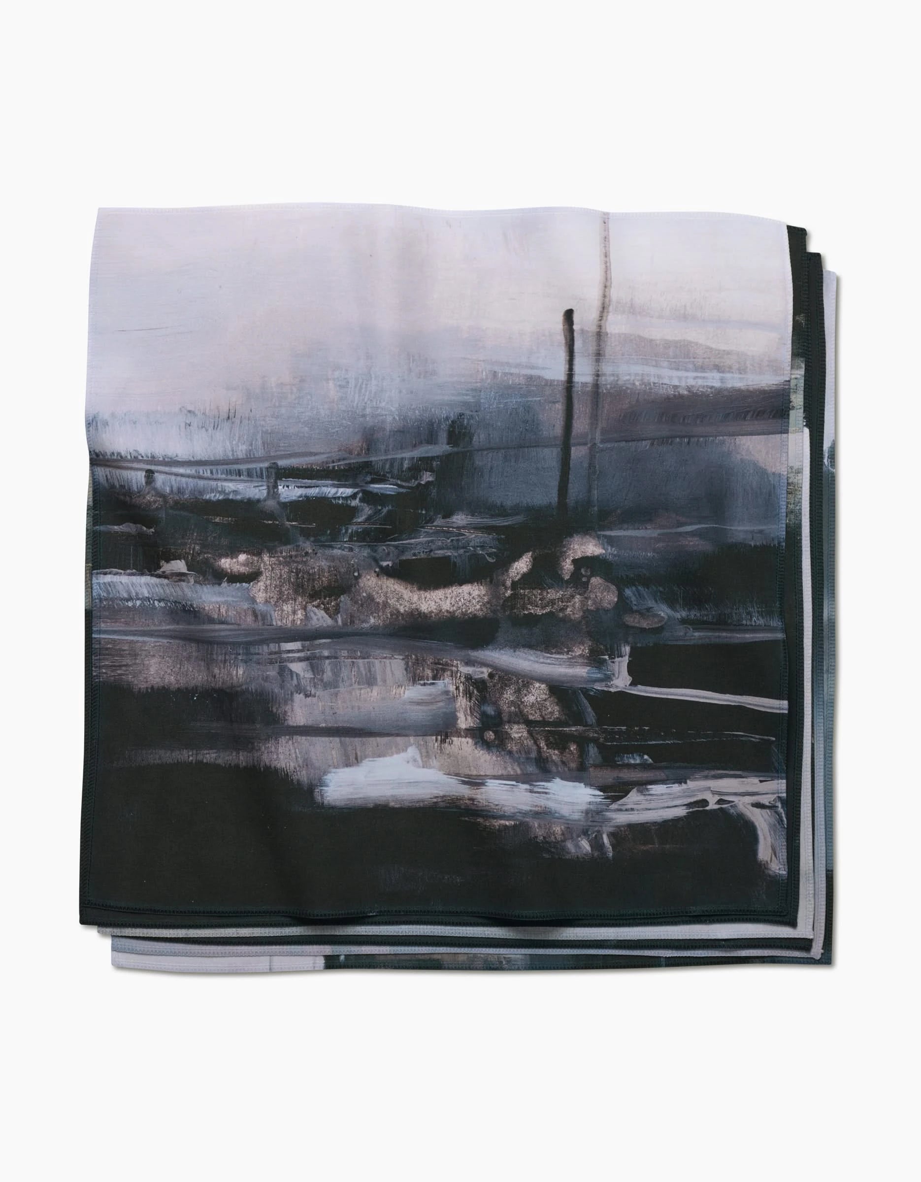 The Icelandic Elements dinner napkin by Jennifer Janesko features Geosuede fabric with an abstract brushstroke design in black, gray, and white, creating a moody, modern landscape on a crisp white background.