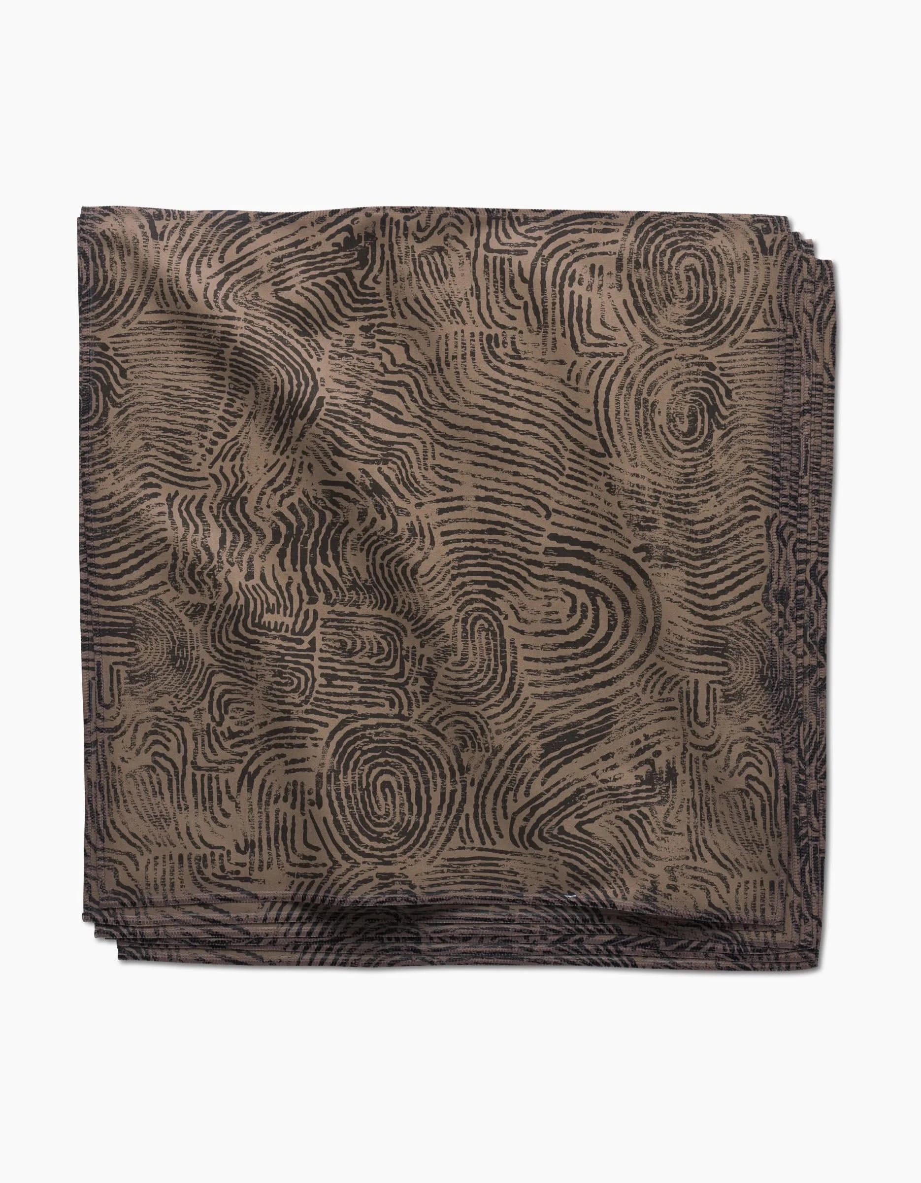 The Imprint Dinner Napkin Set by Studio Jeannot features folded square napkins in Geosuede fabric with a brown base and black abstract maze-like lines, displayed on a white background.
