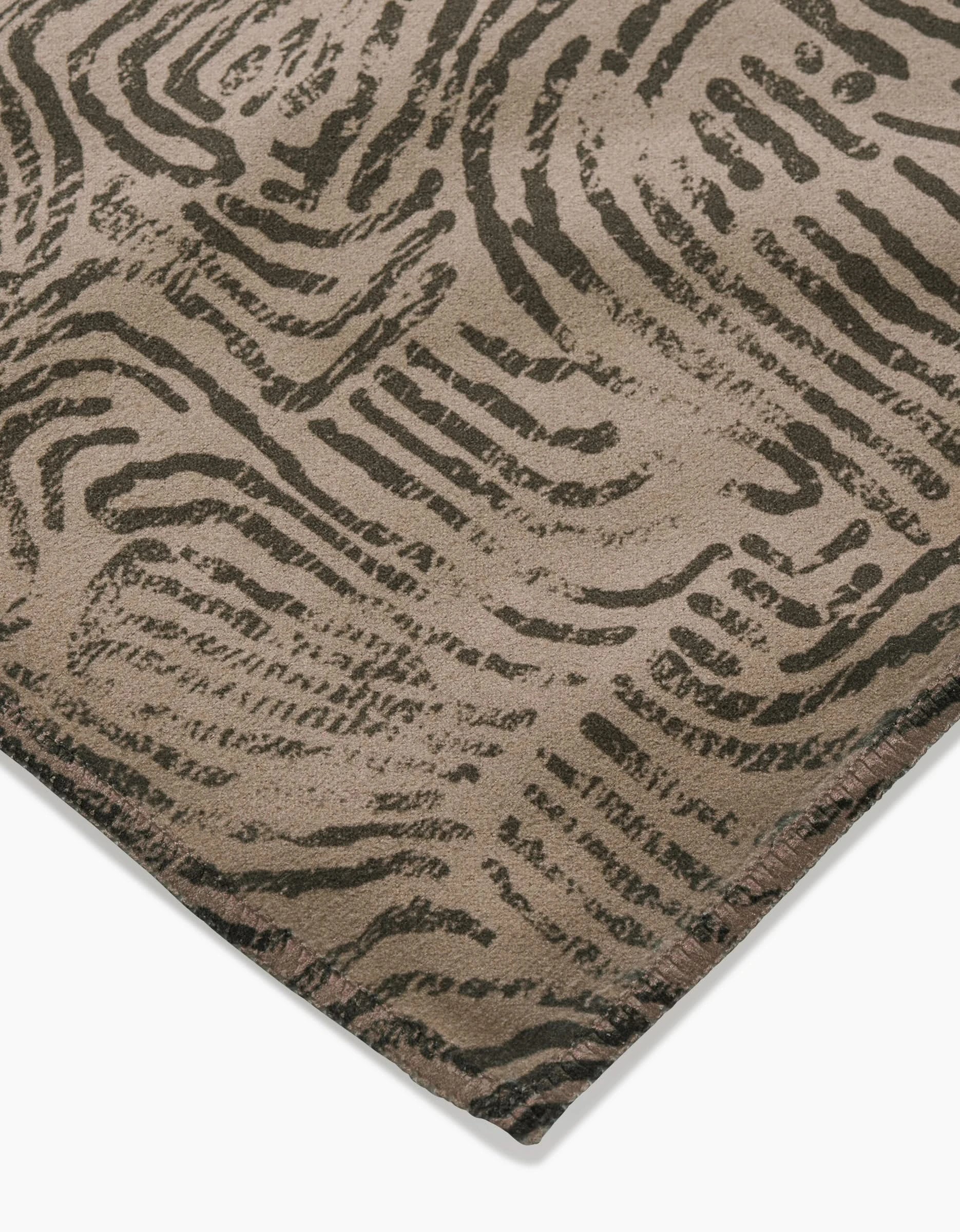 A close-up of the Imprint rug by Studio Jeannot, crafted from recycled materials in beige with dark brown abstract wavy lines, resembling wood grain or topographic patterns. The image highlights the rug’s corner against a white background.