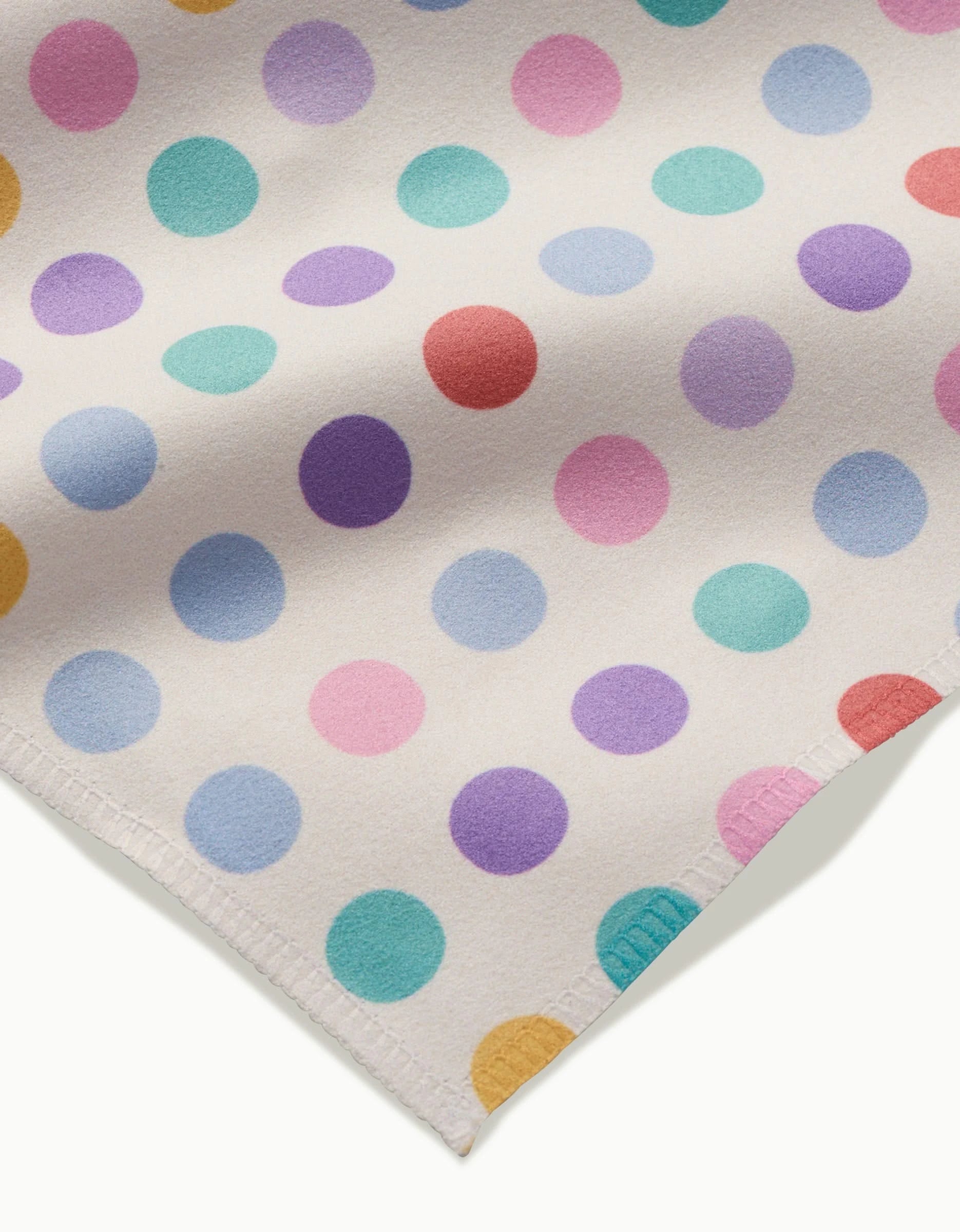 The Lots of Dots napkin by Rebecca Bobko features white Geosuede fabric adorned with pastel polka dots—purple, pink, blue, yellow, red—and stitched edges, making it perfect for stylish dinner napkin sets.