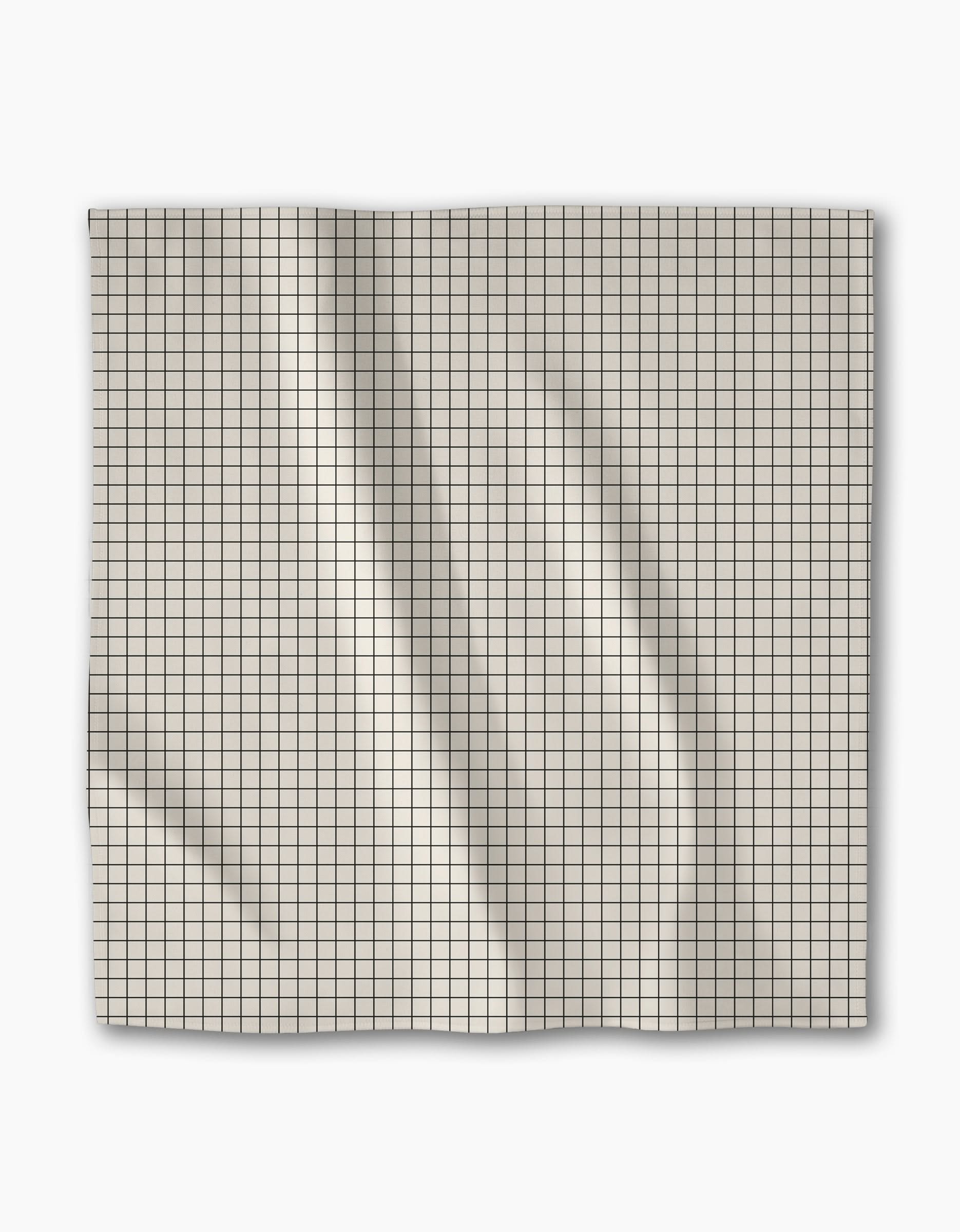 The Geometry Metro Grid dinner napkin features light-colored Geosuede fabric in a square shape with a small black grid pattern, displayed flat on a white background showing creases and folds.
