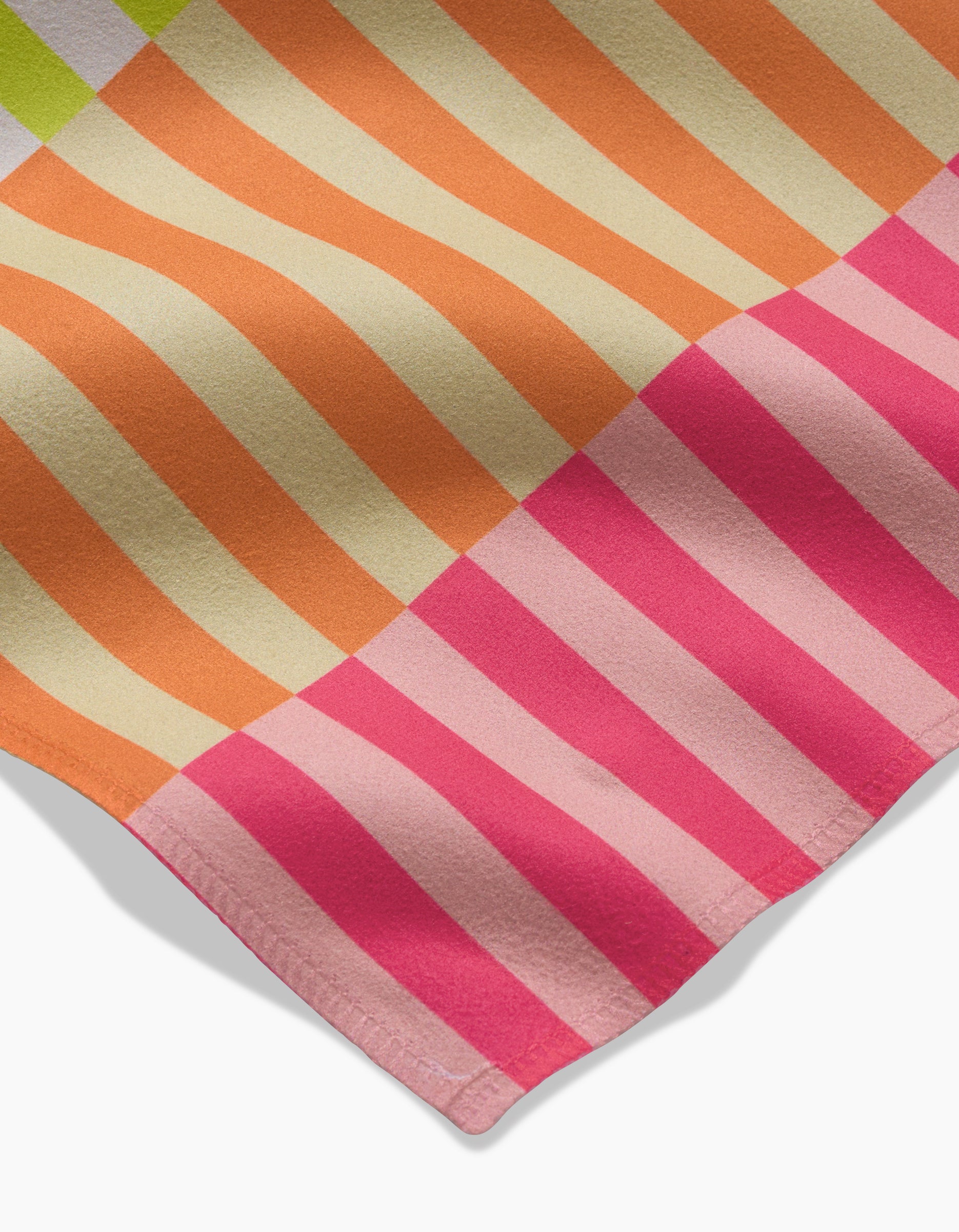 A close-up of GEOMETRY’s Neon Nights Geosuede fabric shows diagonal orange and cream stripes fading to pink, a hemmed edge, and a shadow on white—perfect for eco-friendly Dinner Napkins crafted from recycled materials.