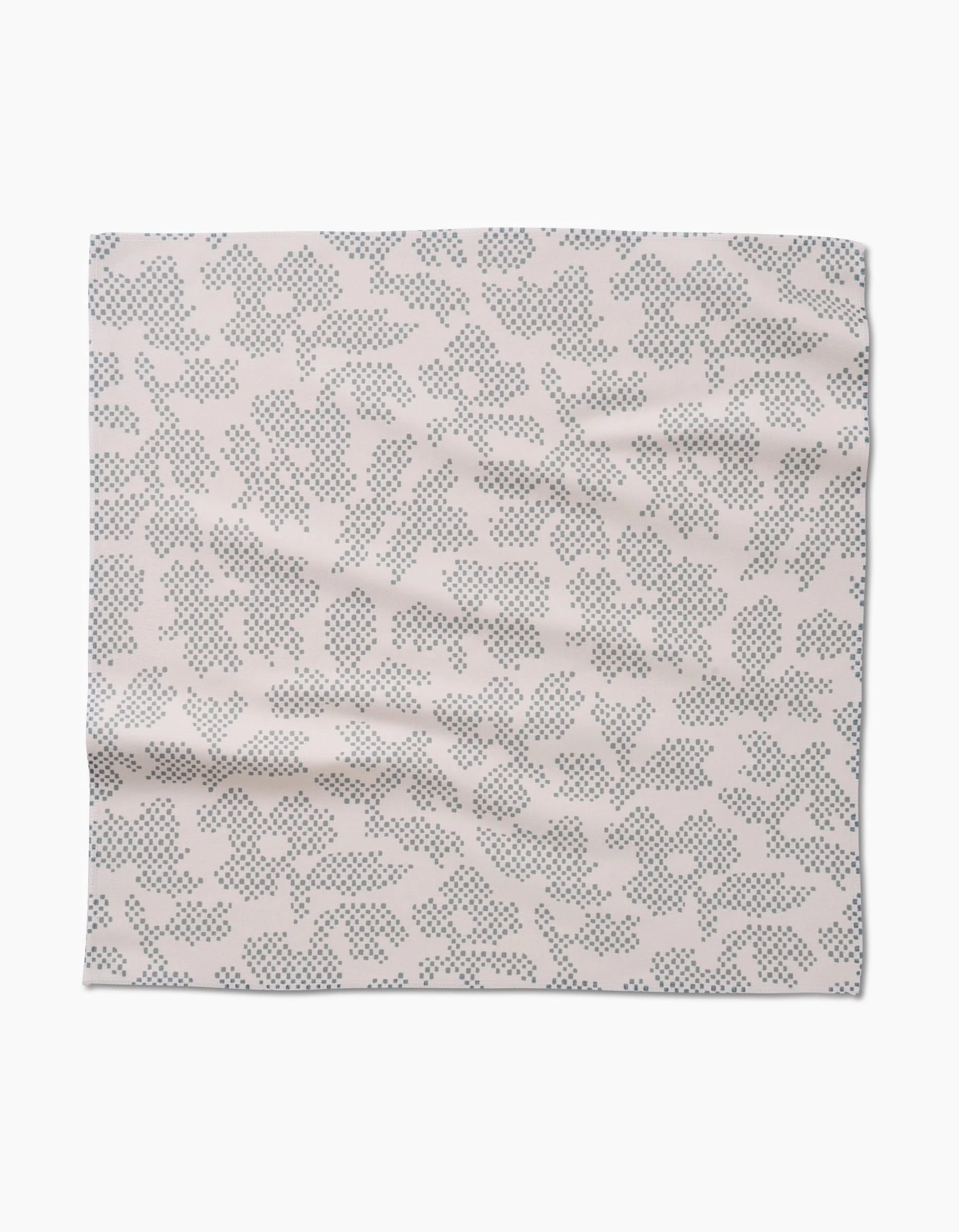 The Pixie Sage napkin set by Studio Jeannot features square Geosuede fabric in light beige with abstract black dot, leaf-like patterns. Laid flat with gentle wrinkles, these are crafted from recycled materials.