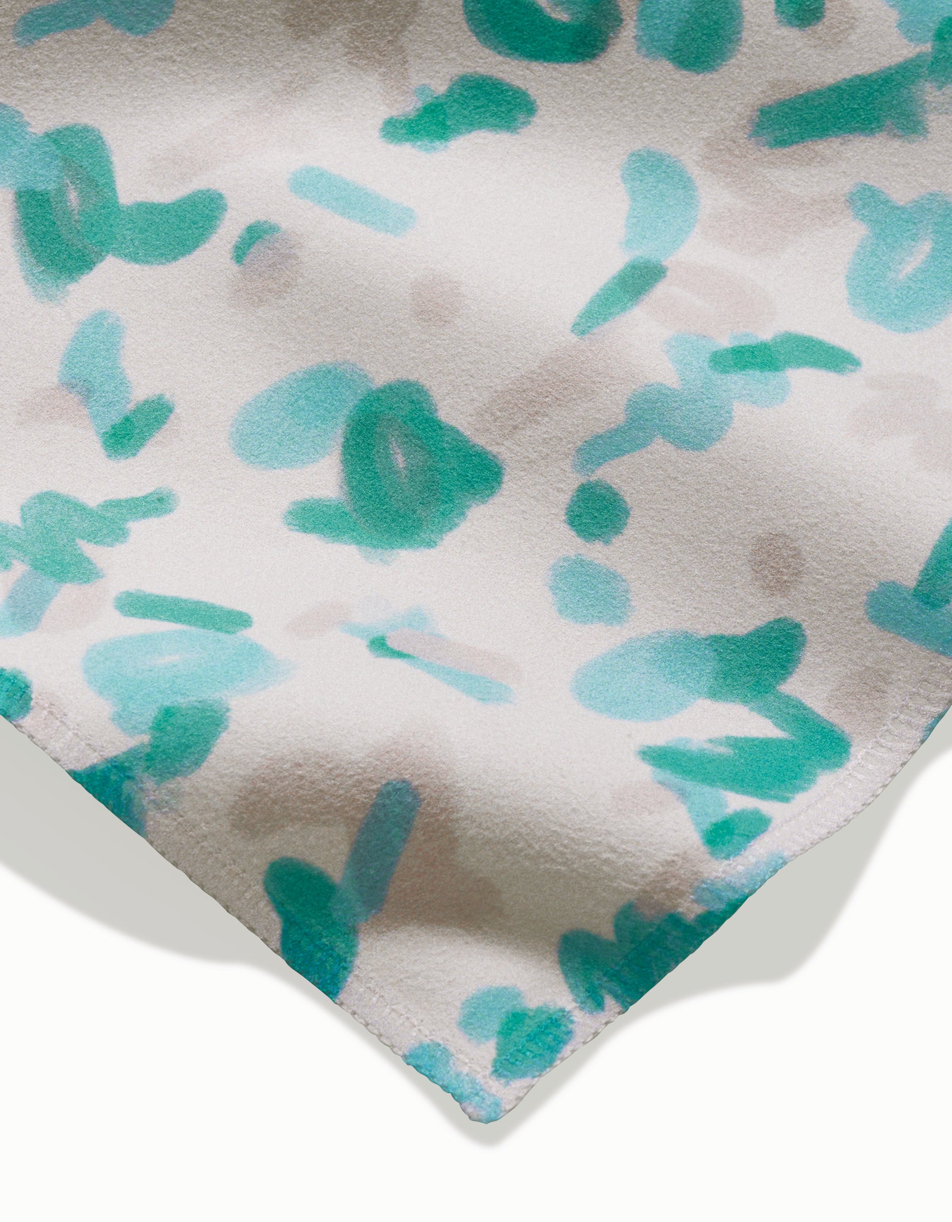 A close-up of GEOMETRY’s “Playful Blues” napkin shows eco-friendly Geosuede fabric with teal brushstrokes and pale gray spots on white, plus a stitched edge—ideal for dinner napkins.