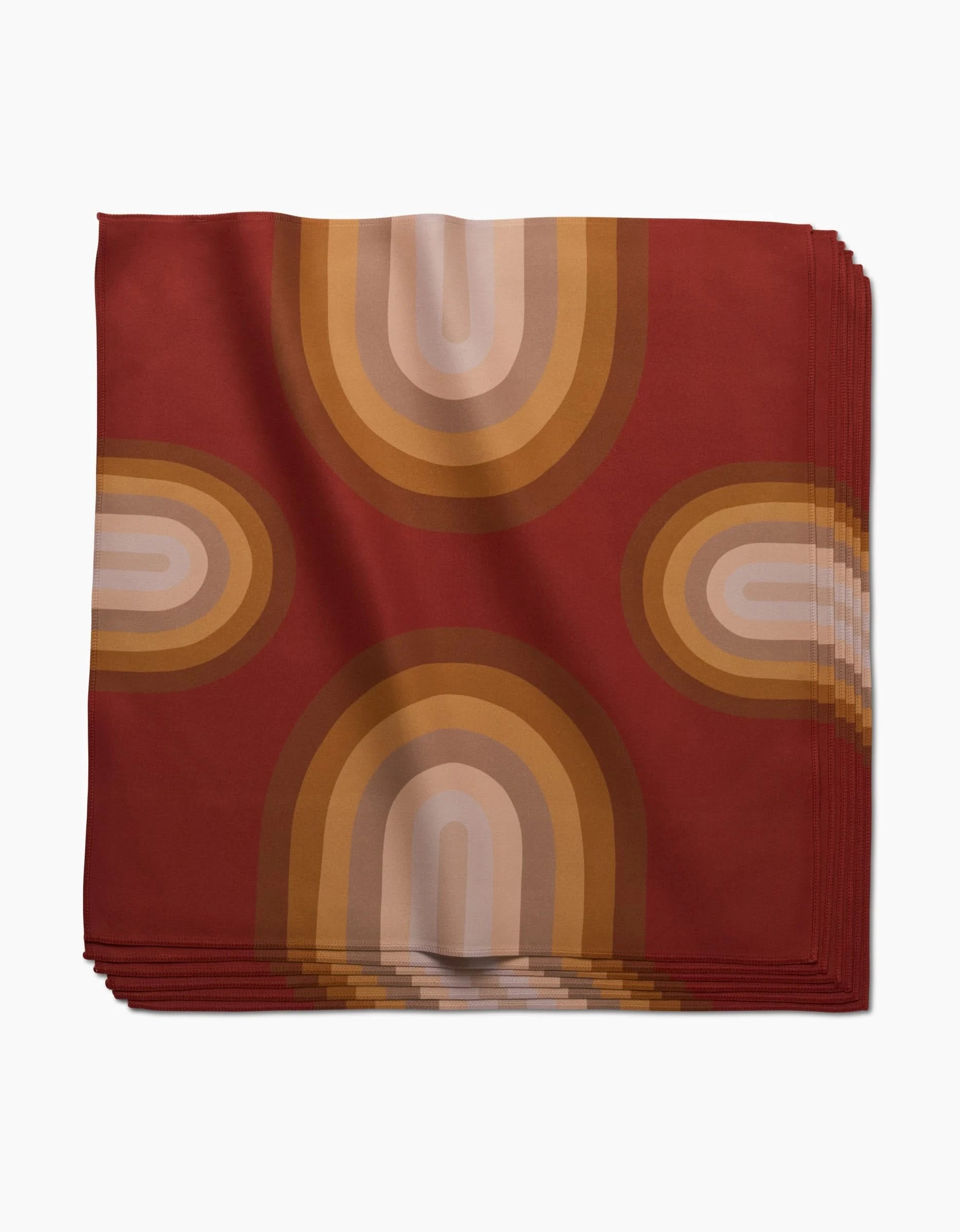 A folded red absorbent cloth napkin, Pumpkin Spice by GEOMETRY, features a retro geometric arch pattern in brown, beige, and gold with a symmetrical design.