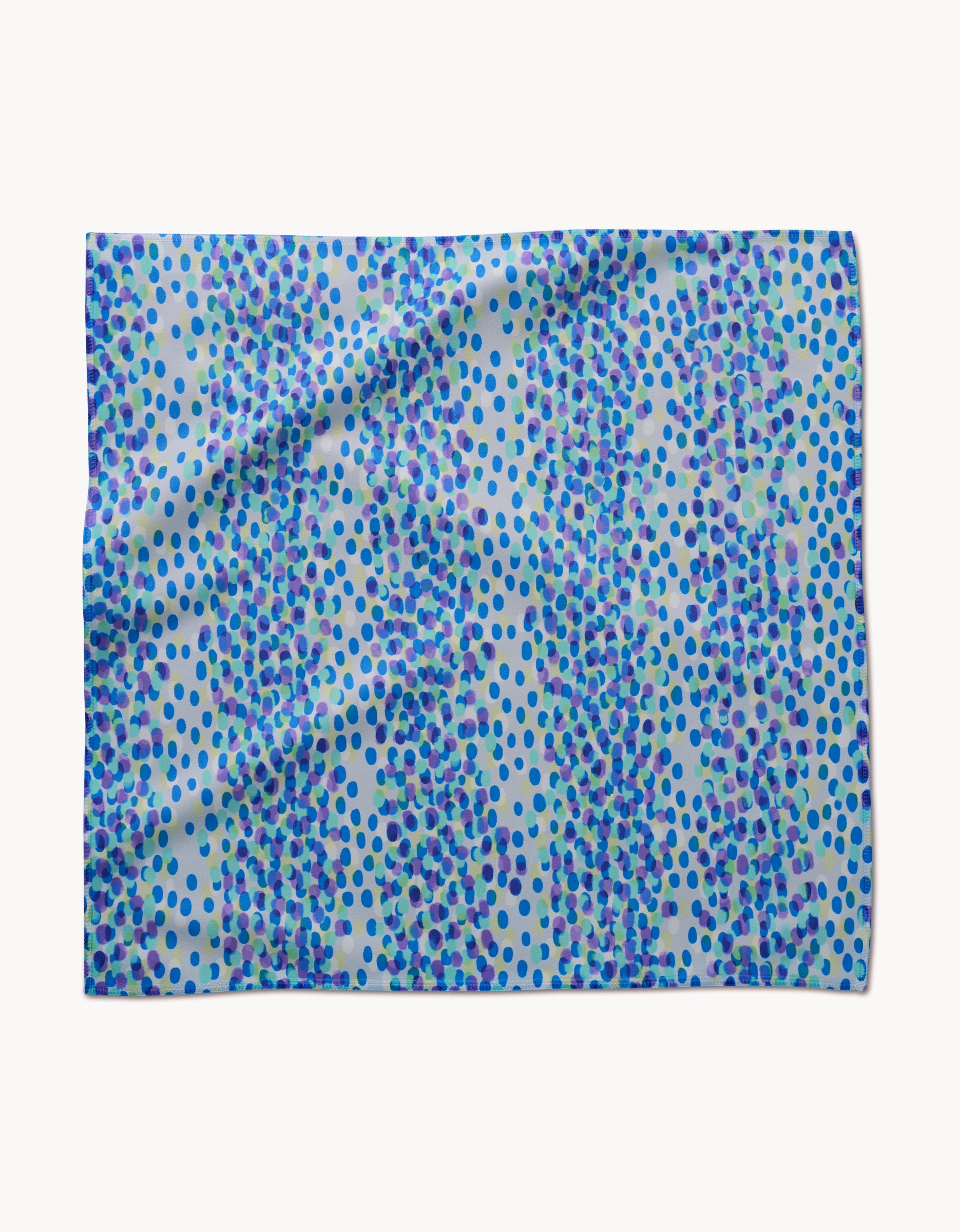 The GEOMETRY Spotty Summer napkin features a vibrant, abstract polka dot design in blue, turquoise, and purple on a light background. Its absorbent fabric with slight folds is perfect for adding color to any dinner setting.