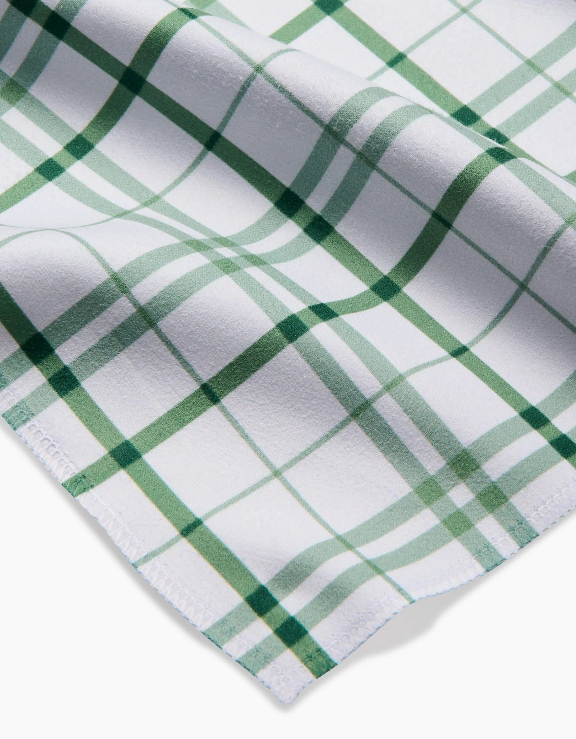 A close-up of Hufton Studio’s Spring Picnic Plaid napkin set shows white Geosuede fabric with a green plaid pattern, intersecting lines, a soft texture, and one edge finished with a zigzag cut.