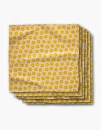 A stack of Sunny Sun beige eco-friendly napkins by Geometry, featuring a repeated yellow sunburst pattern, neatly arranged on a white background.