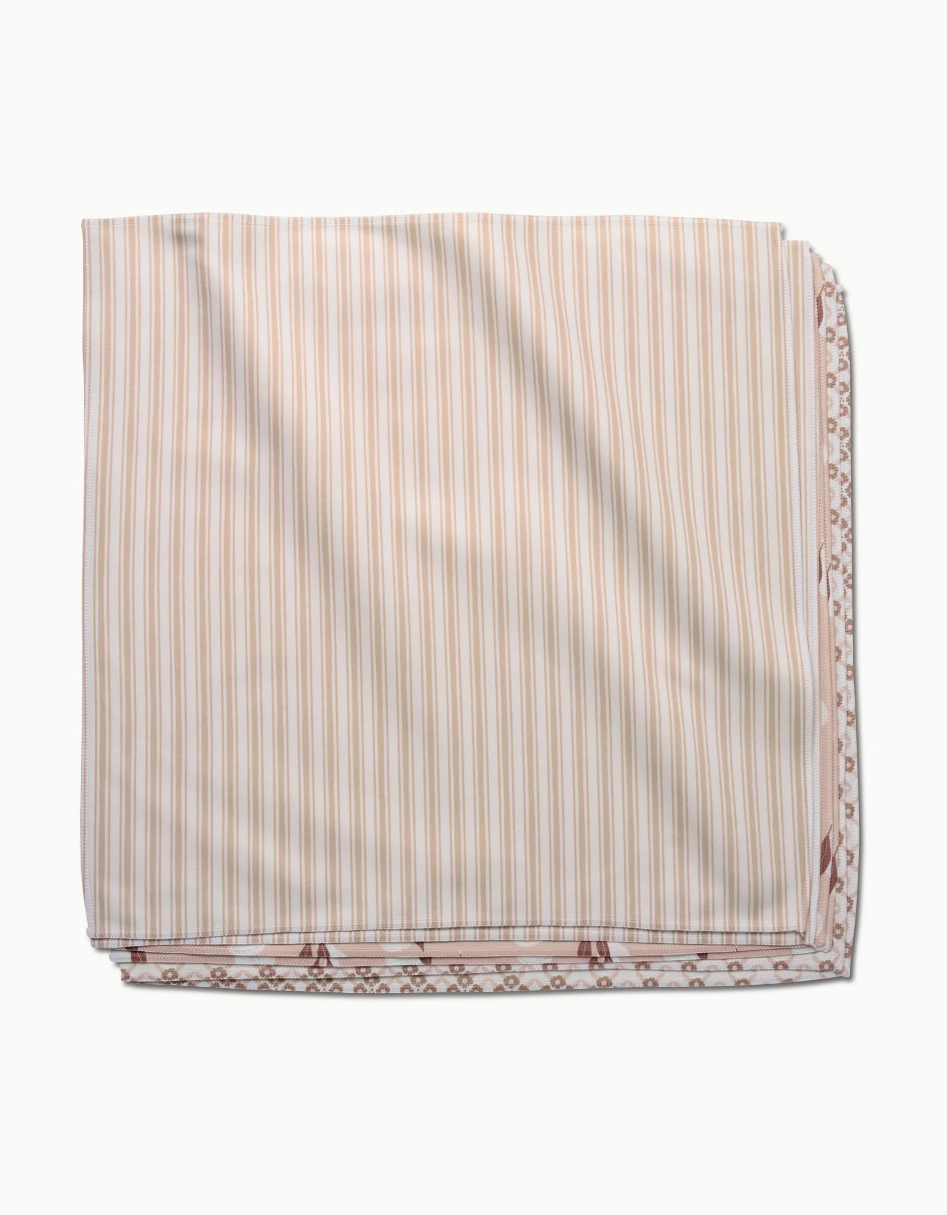 The Sweet Boho dinner napkin set by Hufton Studio is displayed folded, featuring beige and white vertical stripes on top with hints of a brown and white pattern peeking out at the edges.