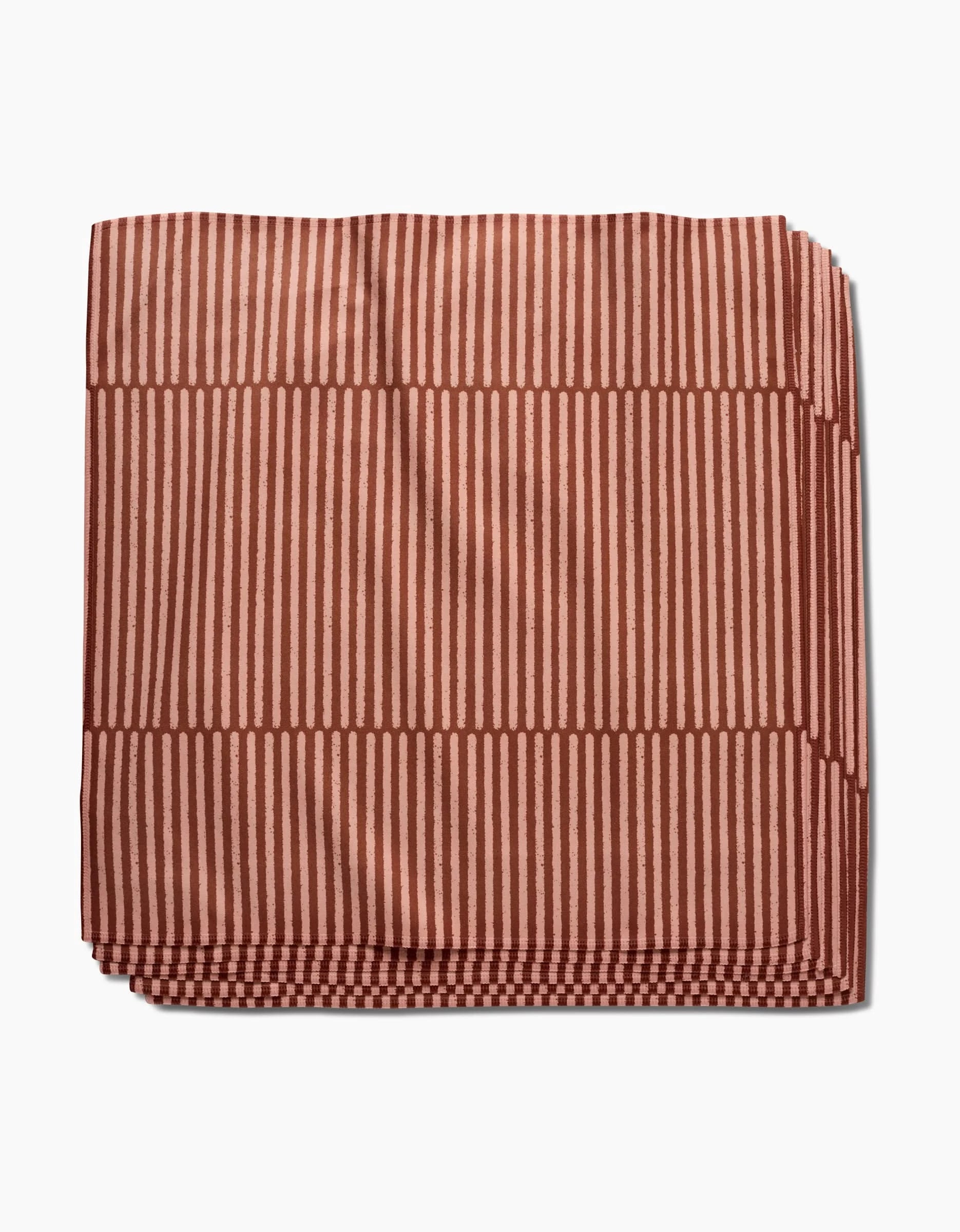 The Rosa Kichline Textured Stripe blanket, crafted from Geosuede Fabric, features a geometric pattern of reddish-brown vertical and horizontal stripes on a light brown background and is shown folded on a white surface.