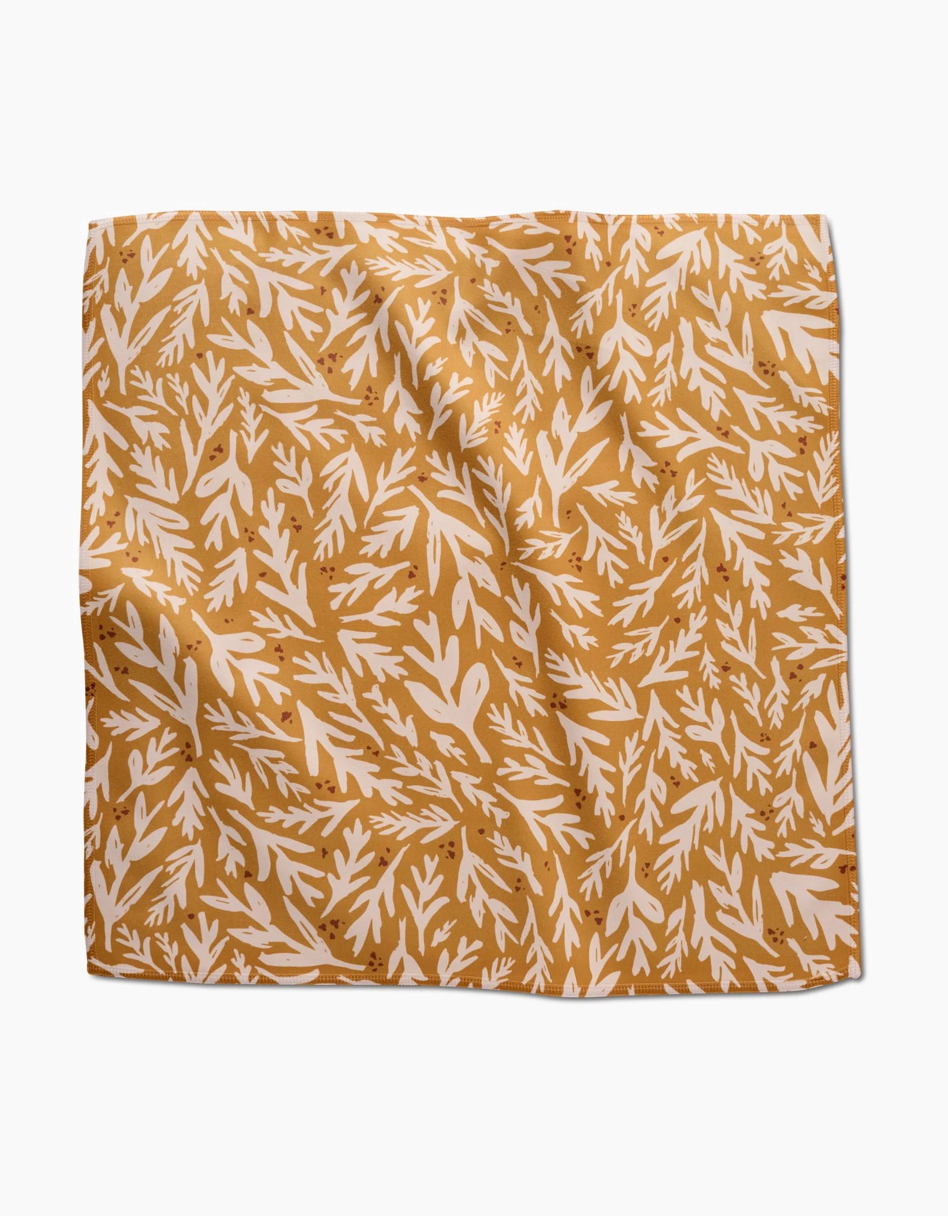 The Trail Dusting Gold napkin by Twig + Spark is a square, recycled cloth with a mustard yellow background and white leafy branch pattern. The absorbent napkin has a slightly wrinkled texture and is shown on a white surface.