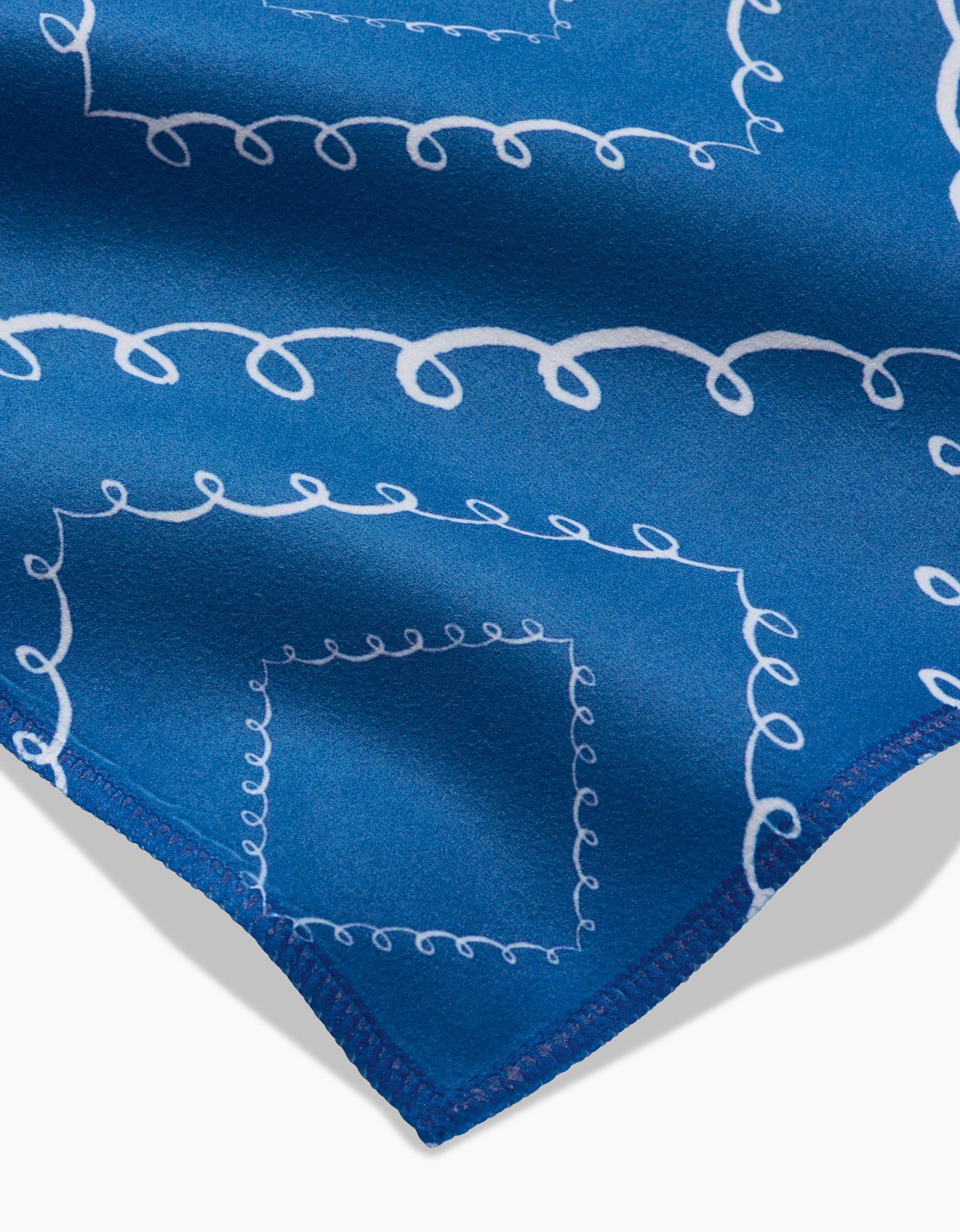 A close-up of Elena Fay’s Twirls: blue fabric with white swirling line patterns, neatly stitched edges—ideal for absorbent cloth napkins or a stylish Dinner Napkin Set.