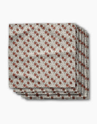 Three folded Wild Dahlia reusable dinner napkins by Geometry, featuring a repeating pattern of red pomegranates and black leafy branches on a beige background, are stacked neatly against a white backdrop.