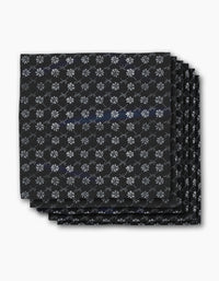 Four neatly stacked Bonnie Indigo napkins by Geometry, featuring a repeating white snowflake-like pattern on black, displayed against a plain white background.