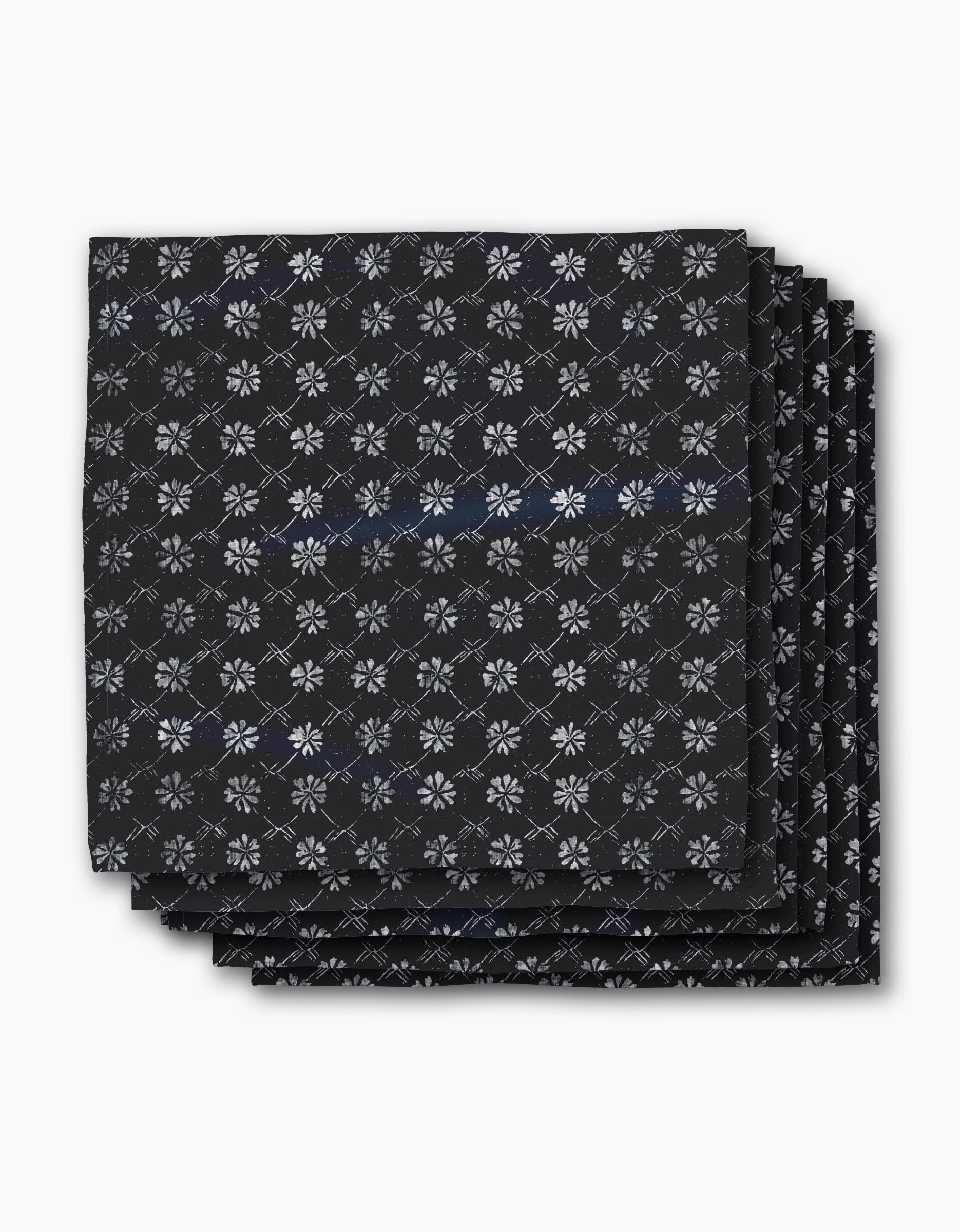 Four neatly stacked Bonnie Indigo napkins by Geometry, featuring a repeating white snowflake-like pattern on black, displayed against a plain white background.