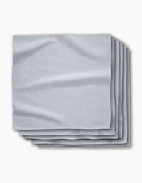 A stack of five Chambray Light Blue absorbent cloth napkins by Geometry is neatly folded on a white background, showcasing their smooth texture and subtle creases.