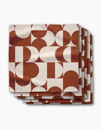 The Circle Playground dinner napkin set by Geometry includes four reusable cloth napkins, each featuring rust red and white geometric shapes on a crisp white background—perfect for adding style to any table setting.