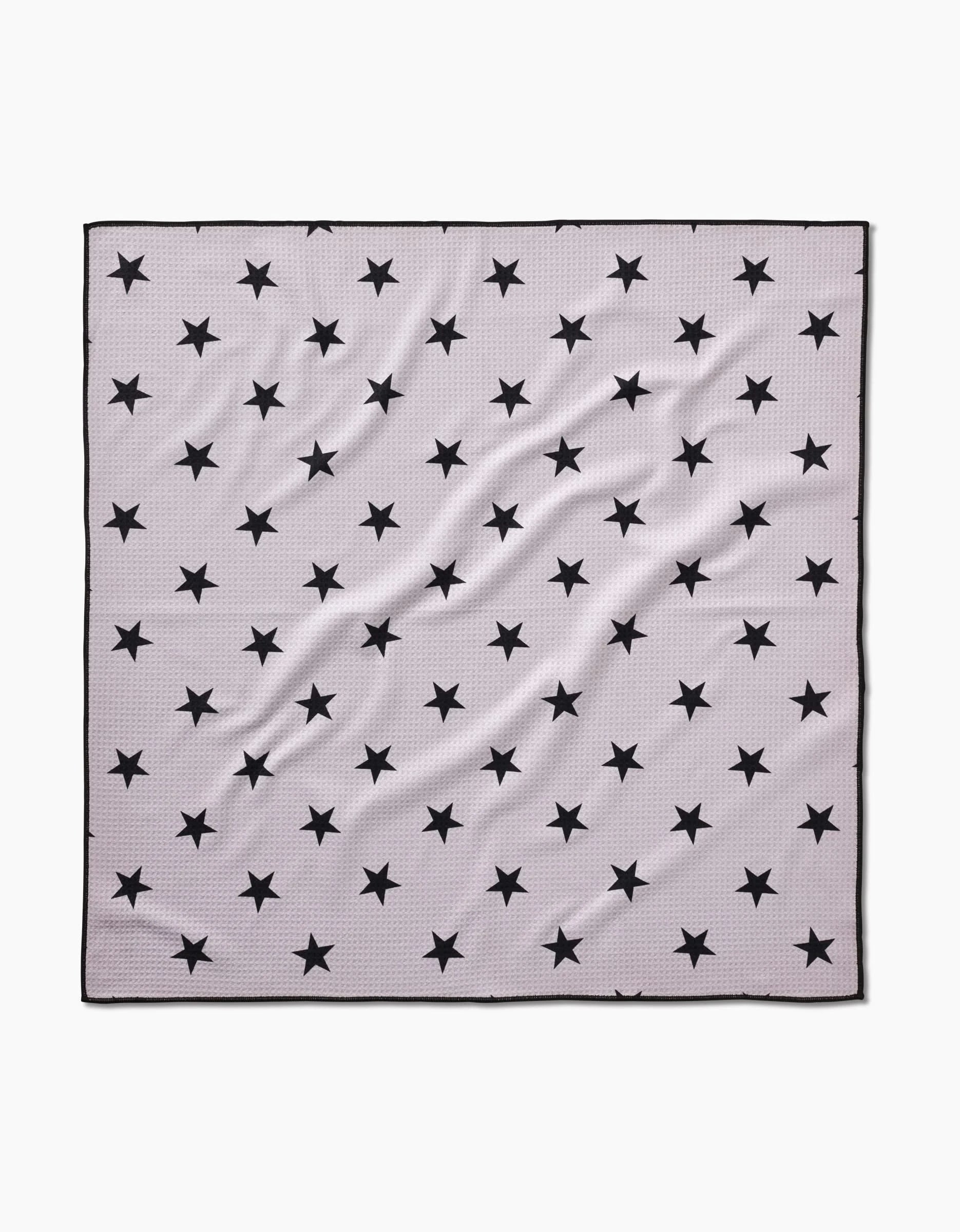 The Bark scarf by Geometry is a square, light gray piece made from recycled materials, featuring a pattern of evenly spaced black stars, a thin black border, and slight fabric wrinkles.