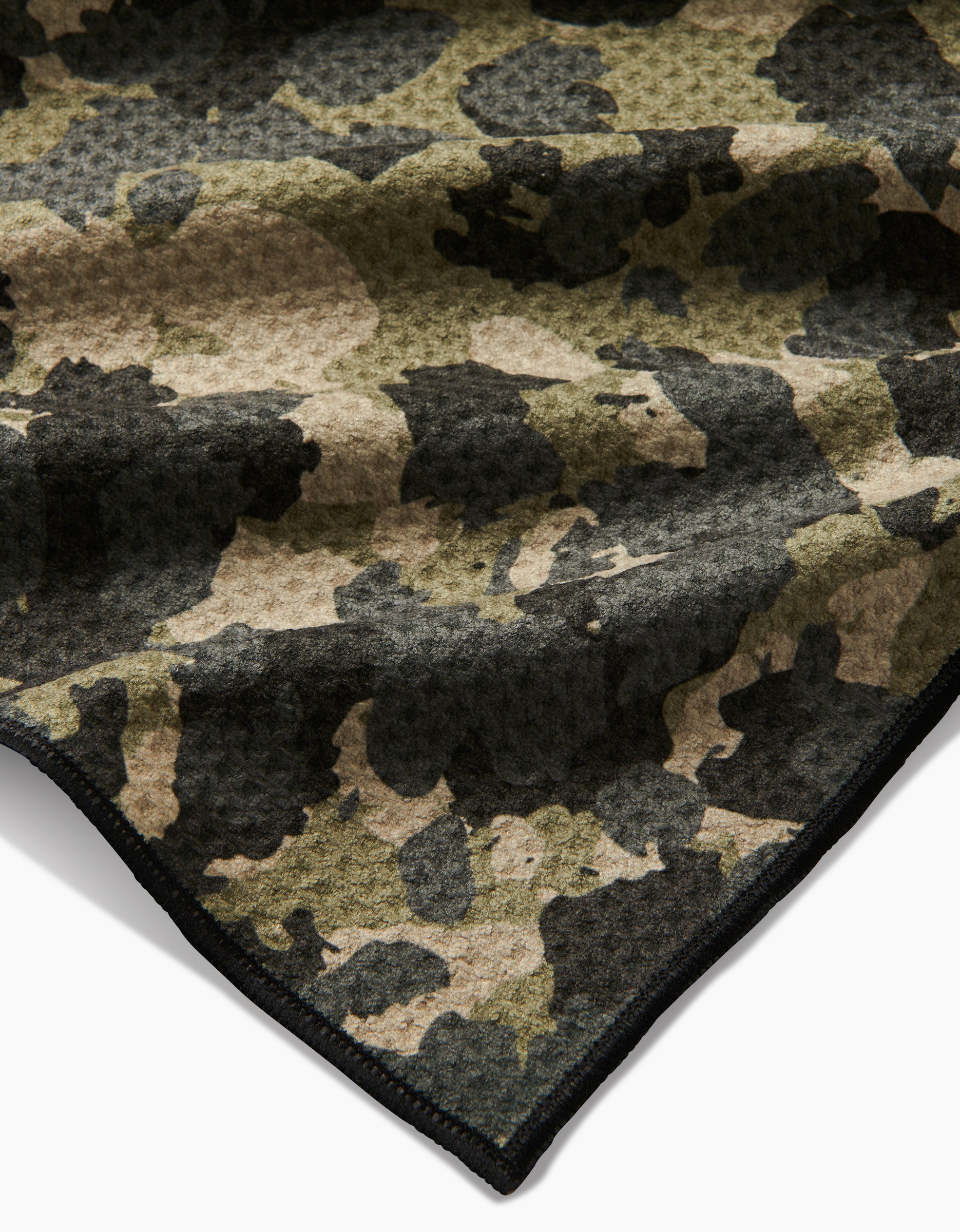 A close-up of Geometry’s Camo dog towel, soft and absorbent with a green, brown, and black camouflage pattern and finished with a black stitched edge.