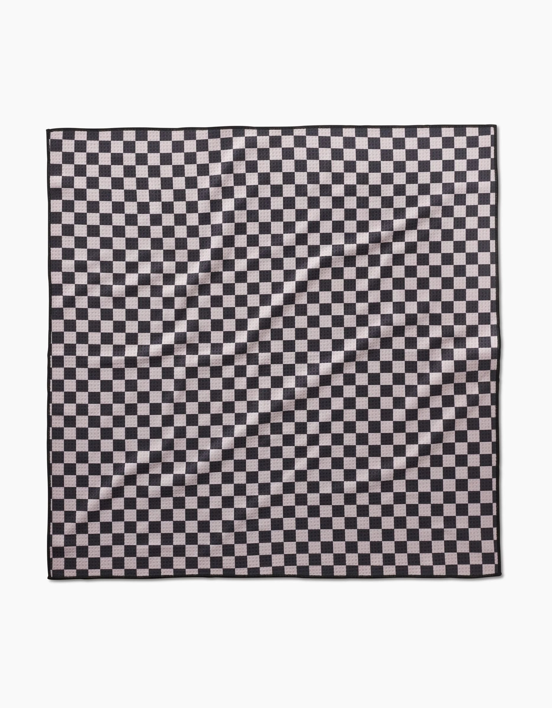 The Geometry Cool Pup dog towel in black and white checkered pattern lays flat, showing a wrinkled, highly absorbent surface with repeating squares.