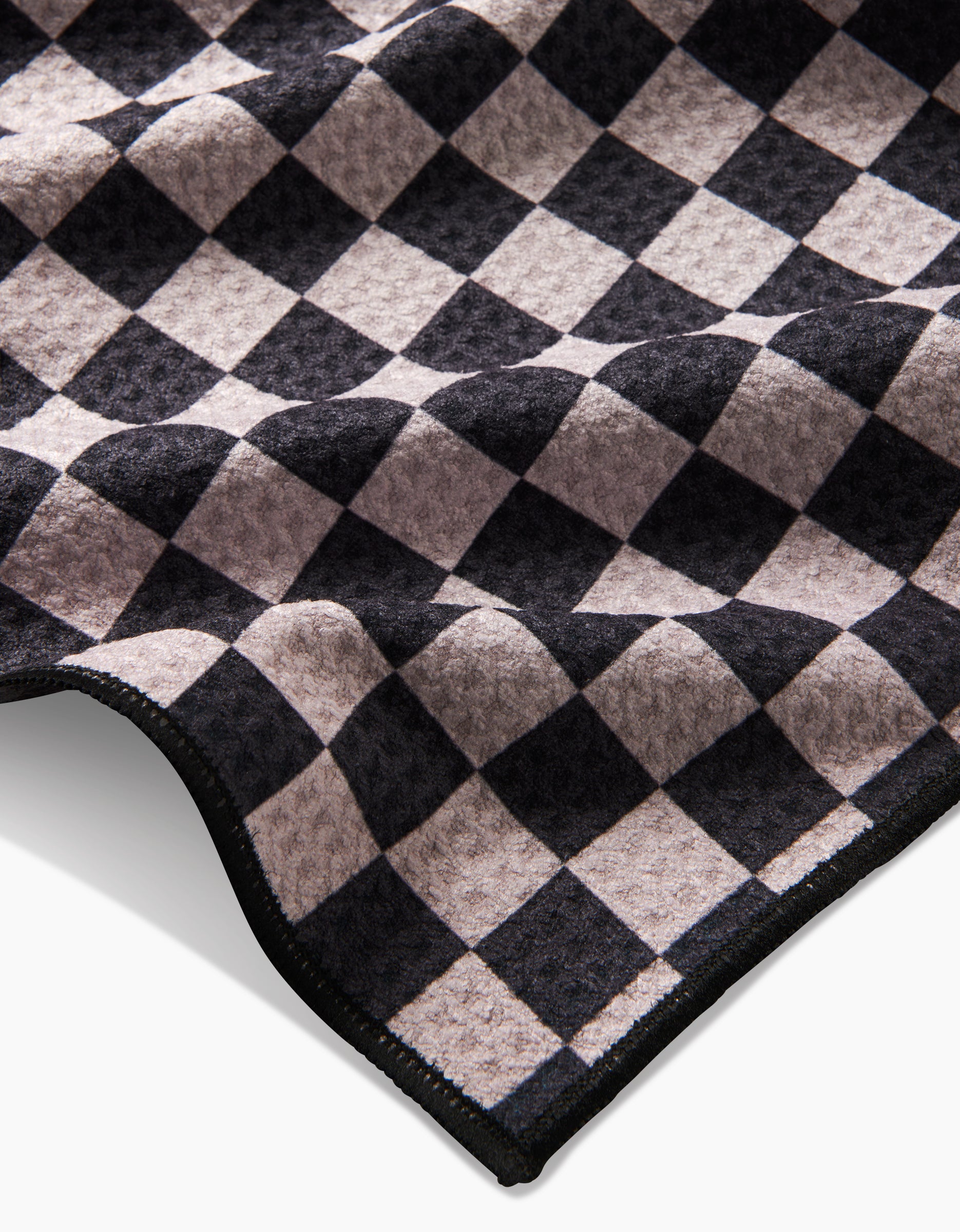 A close-up of the Geometry Cool Pup dog towel, showcasing its black and gray checkered pattern, wavy texture, stitched edge, and eco-friendly construction from recycled materials.
